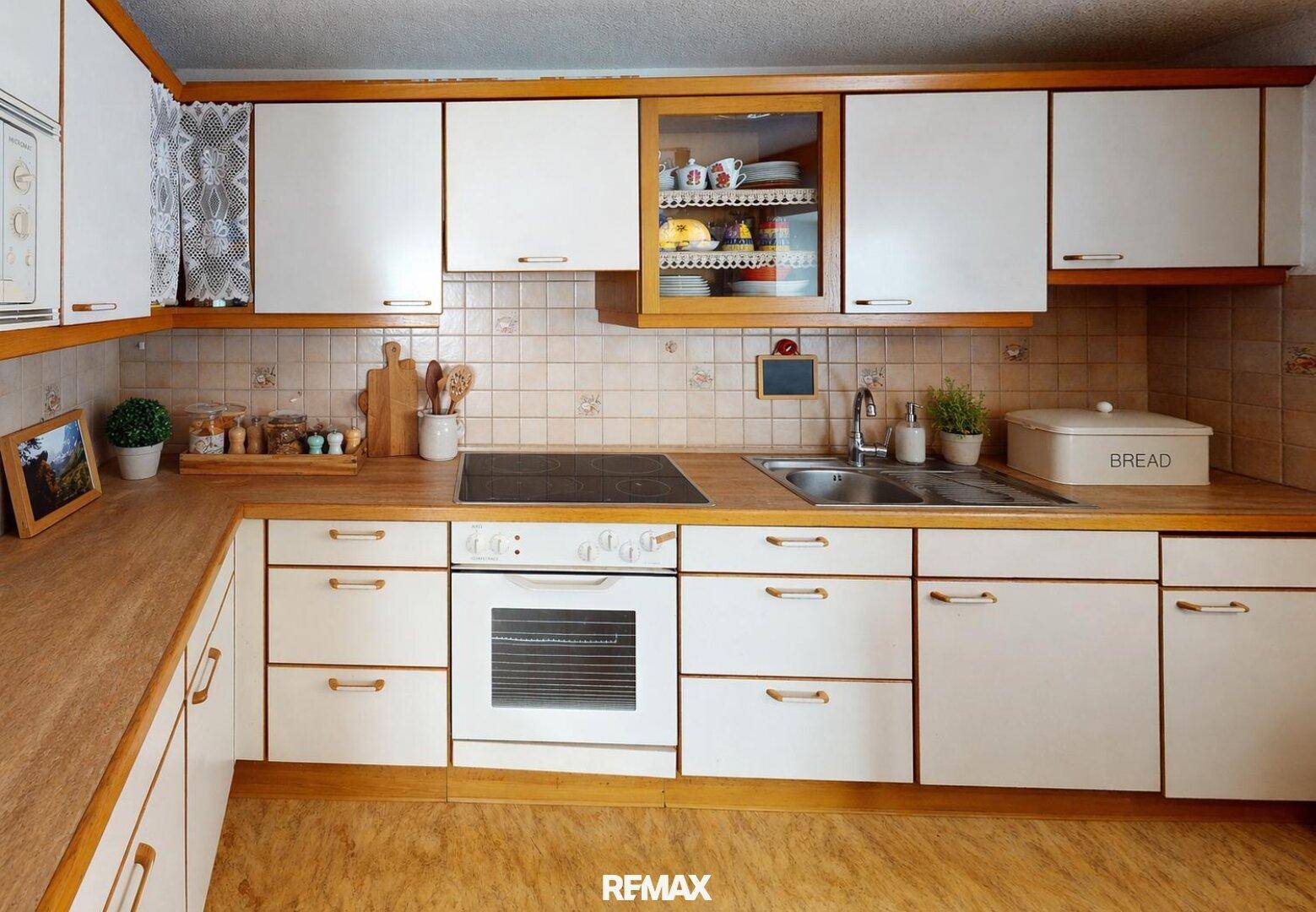 Funktionale Küche mit weißen Schränken, Holzarbeitsplatten, integriertem Kochfeld und Backofen.
