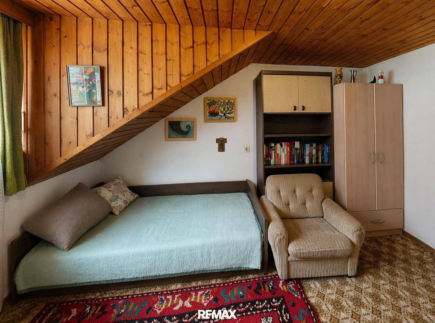 Gemütliches Schlaf- oder Gästezimmer unter einer holzvertäfelten Dachschräge mit Einzelbett und Sessel.