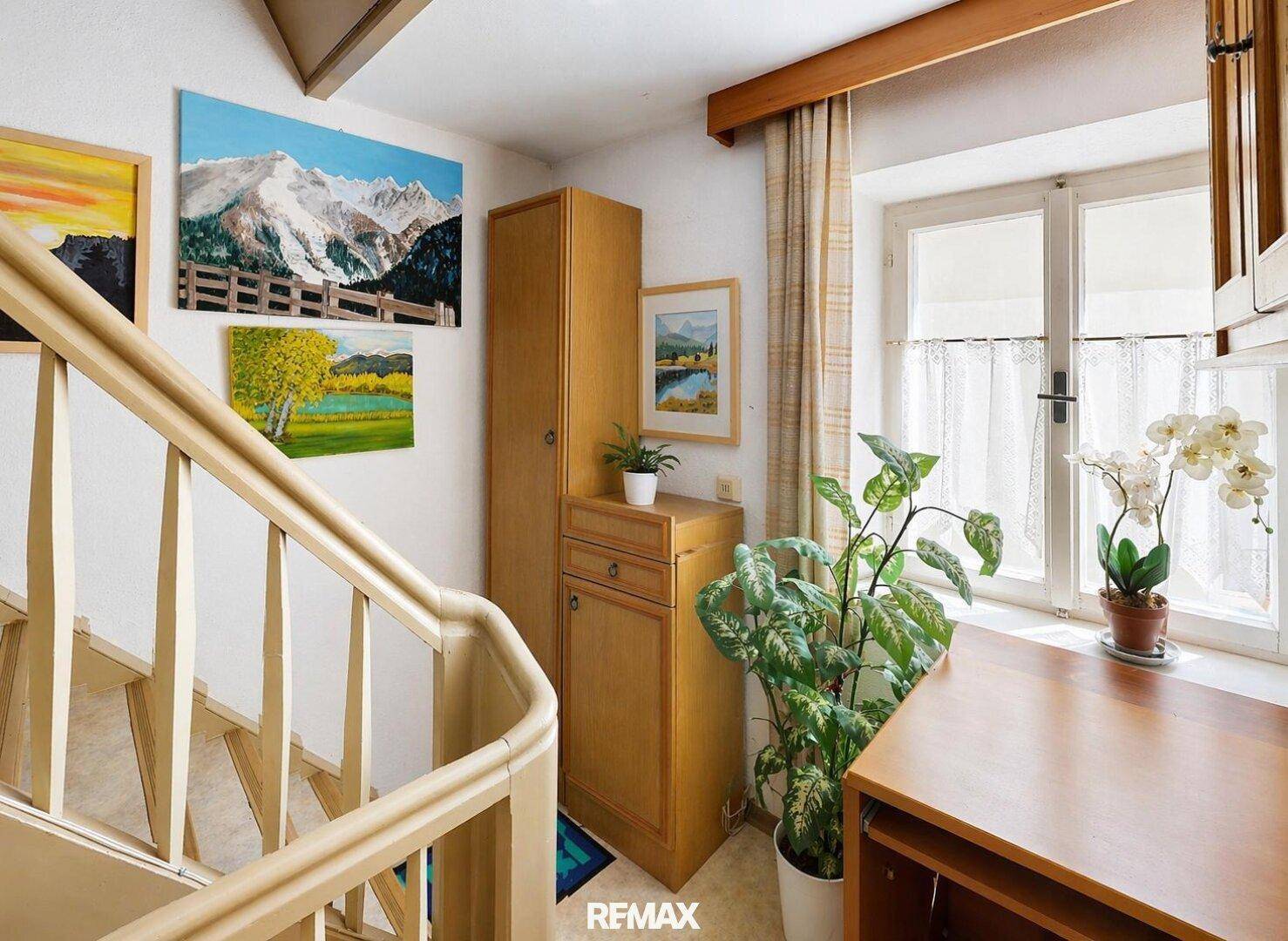 Heller Treppenaufgang mit Holzgeländer, Fenster für Tageslicht, einem Holzschrank und Zimmerpflanzen.