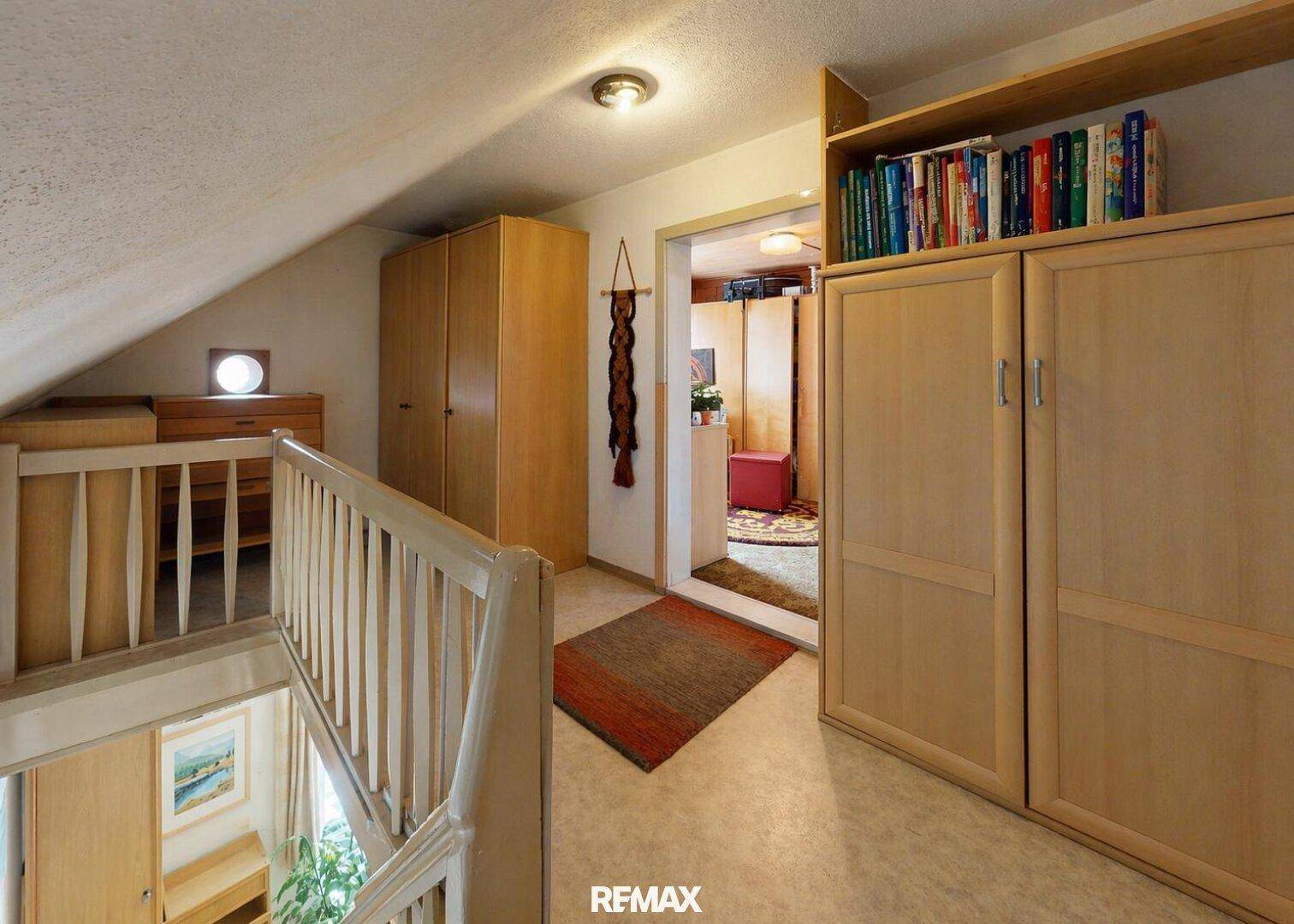 Heller Flur im Obergeschoss mit Treppenabgang, Einbauschränken und einem Bücherregal unter der Dachschräge.