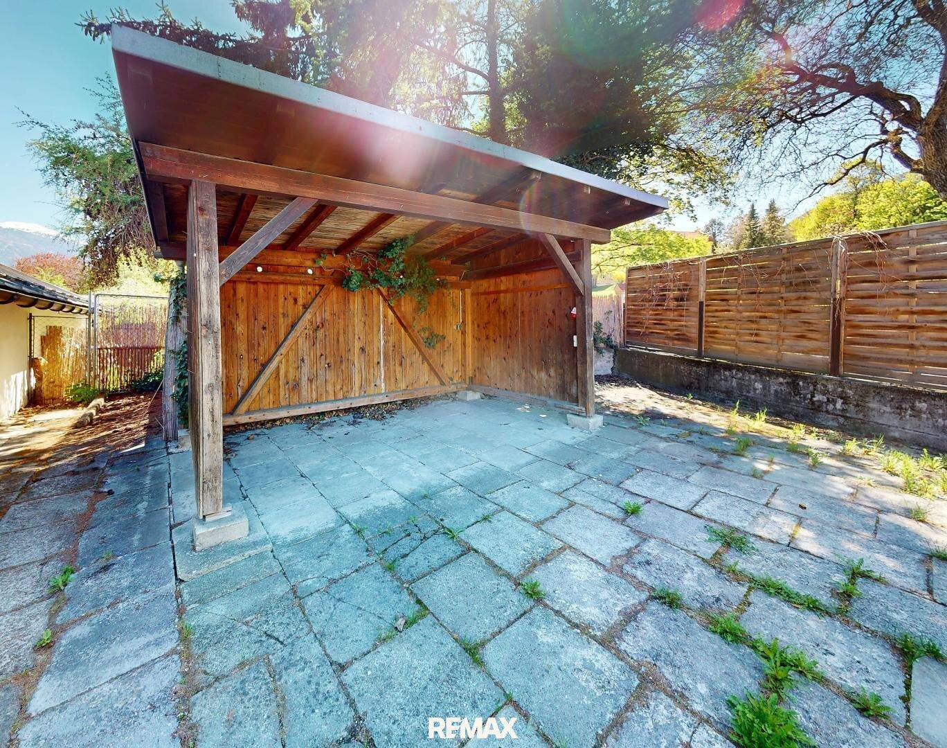 Hölzerner Carport mit gepflastertem Boden und umgebender Vegetation.