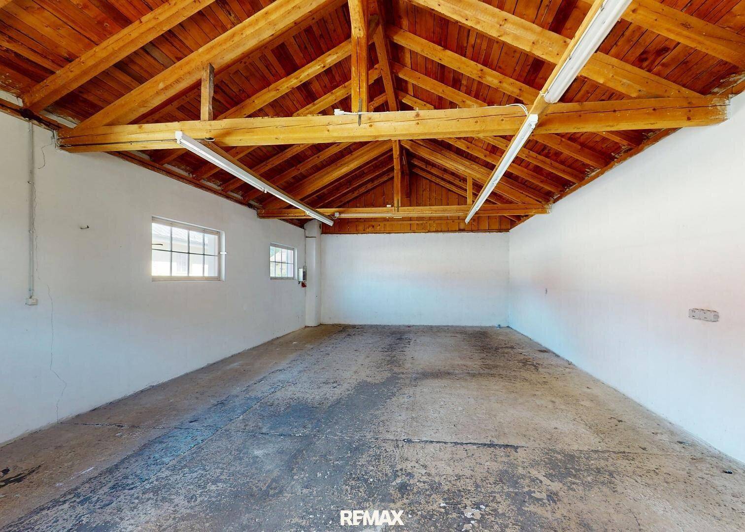 Geräumige Garage mit freiliegender Holz-Dachkonstruktion, Betonboden und hohen Decken.