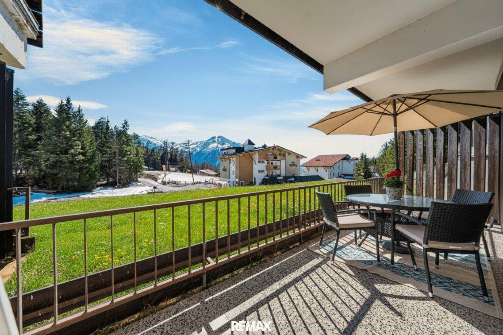 Geräumiger Balkon mit Sitzgelegenheiten, Sonnenschirm und weitem Blick auf die umliegende Berglandschaft.