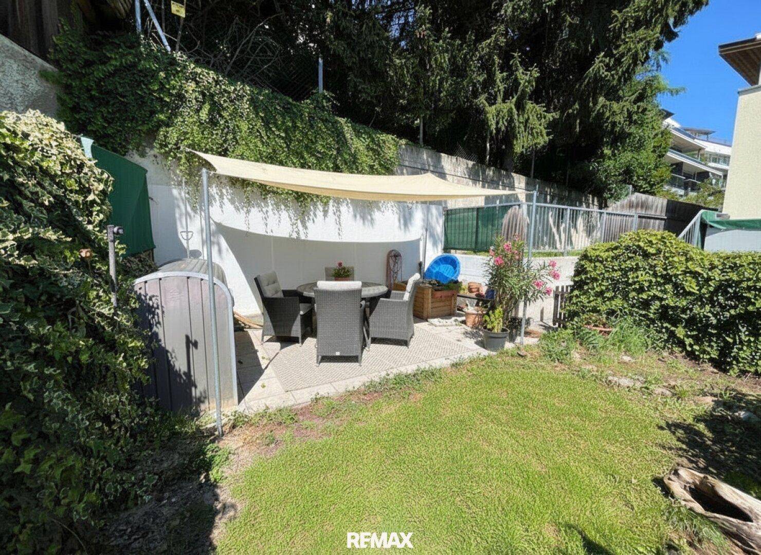 Kleiner Gartenbereich mit schattiger Terrasse, Sitzmöbeln und üppiger Bepflanzung.