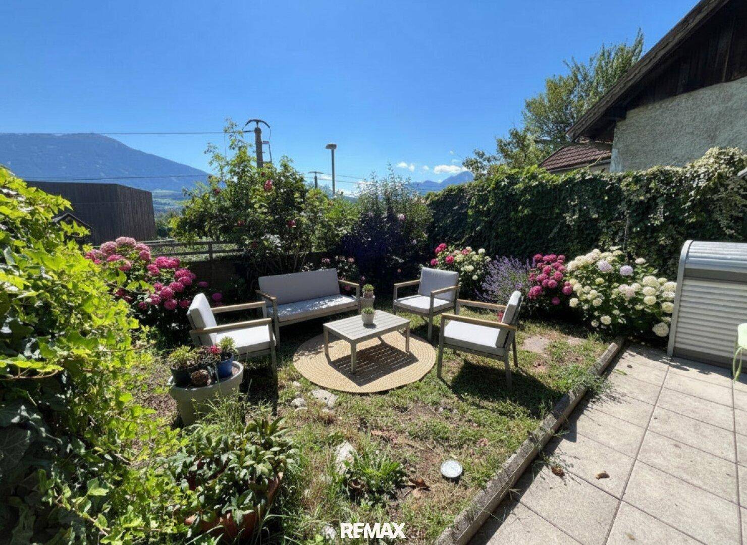 Gepflegter Garten mit Sitzgruppe, Blumenbeeten und Blick auf die umliegende Landschaft.