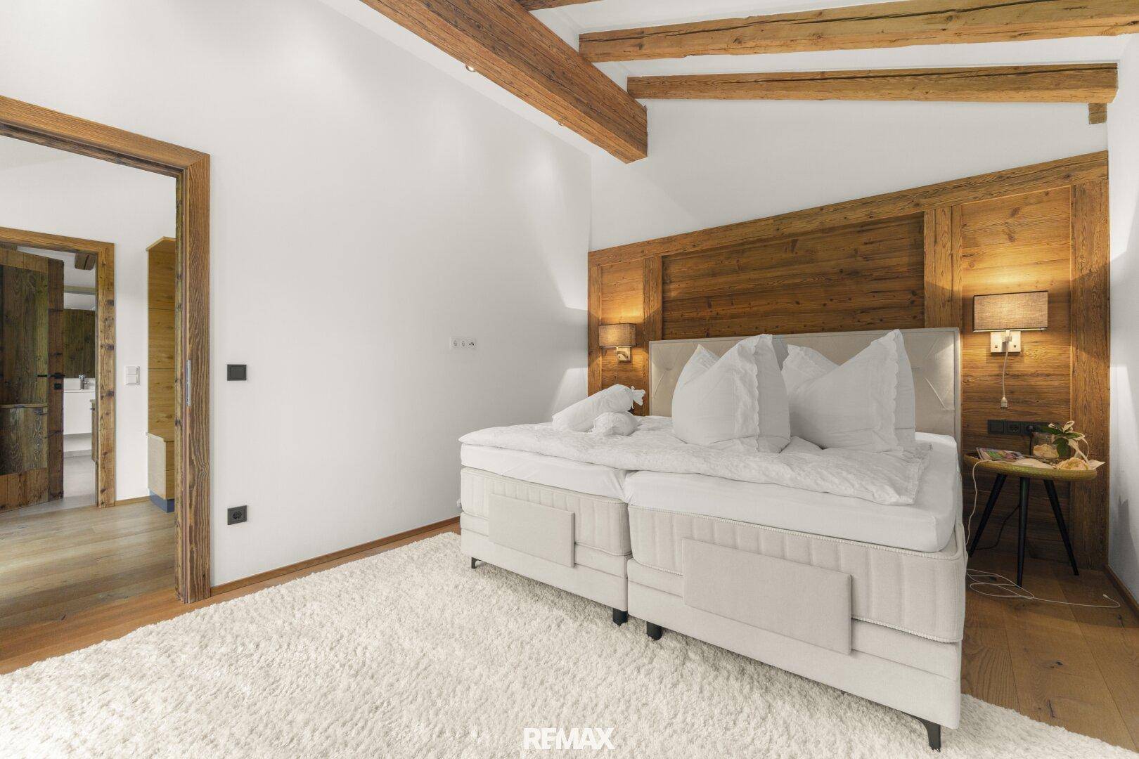 Gemütliches Schlafzimmer mit großem Boxspringbett, Holzwandverkleidung und weichem Teppichboden.