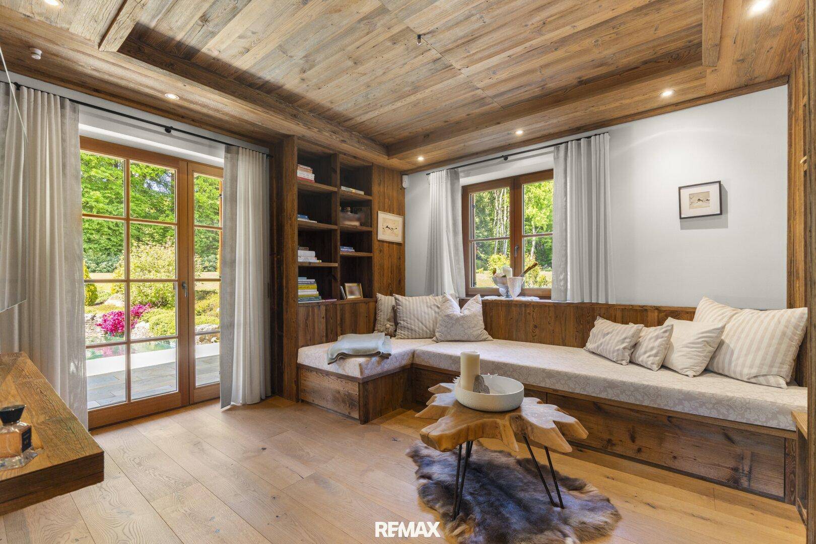 Rustikales Wohnzimmer mit Holzwänden, eingebauten Sitzbänken und Zugang zum Garten.