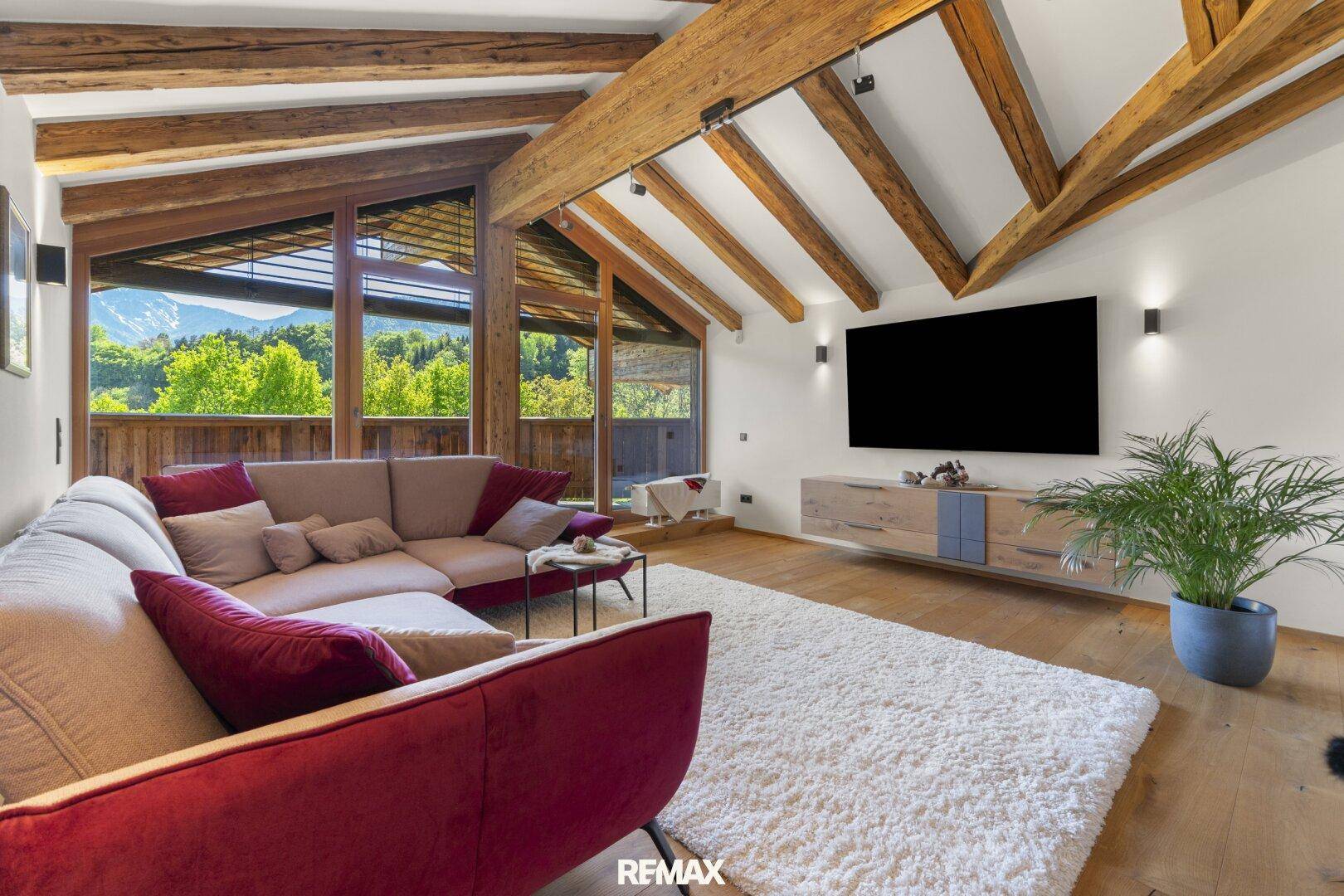 Geräumiges Wohnzimmer mit bequemer Couch, Holzbalkendecke und Panoramablick auf die Berge.