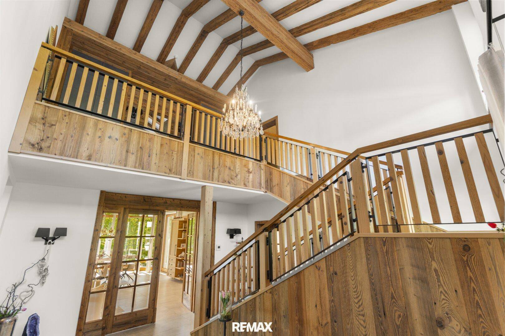 Beeindruckendes Treppenhaus mit Holzgeländer, hohen Decken und sichtbaren Holzbalken.