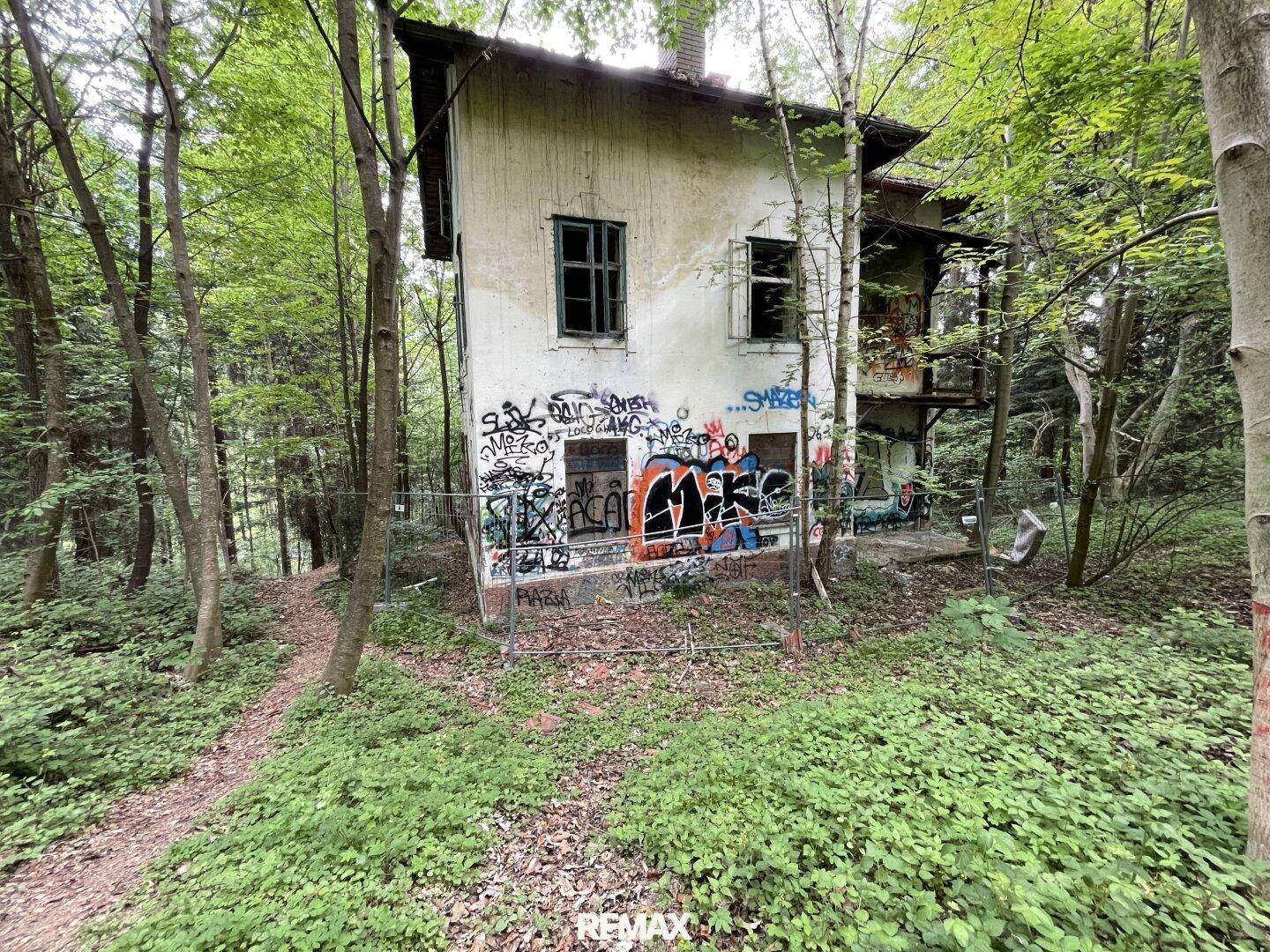 Ansicht des heruntergekommenen Gebäudes mit Graffiti an der Fassade, eingebettet in den Wald.