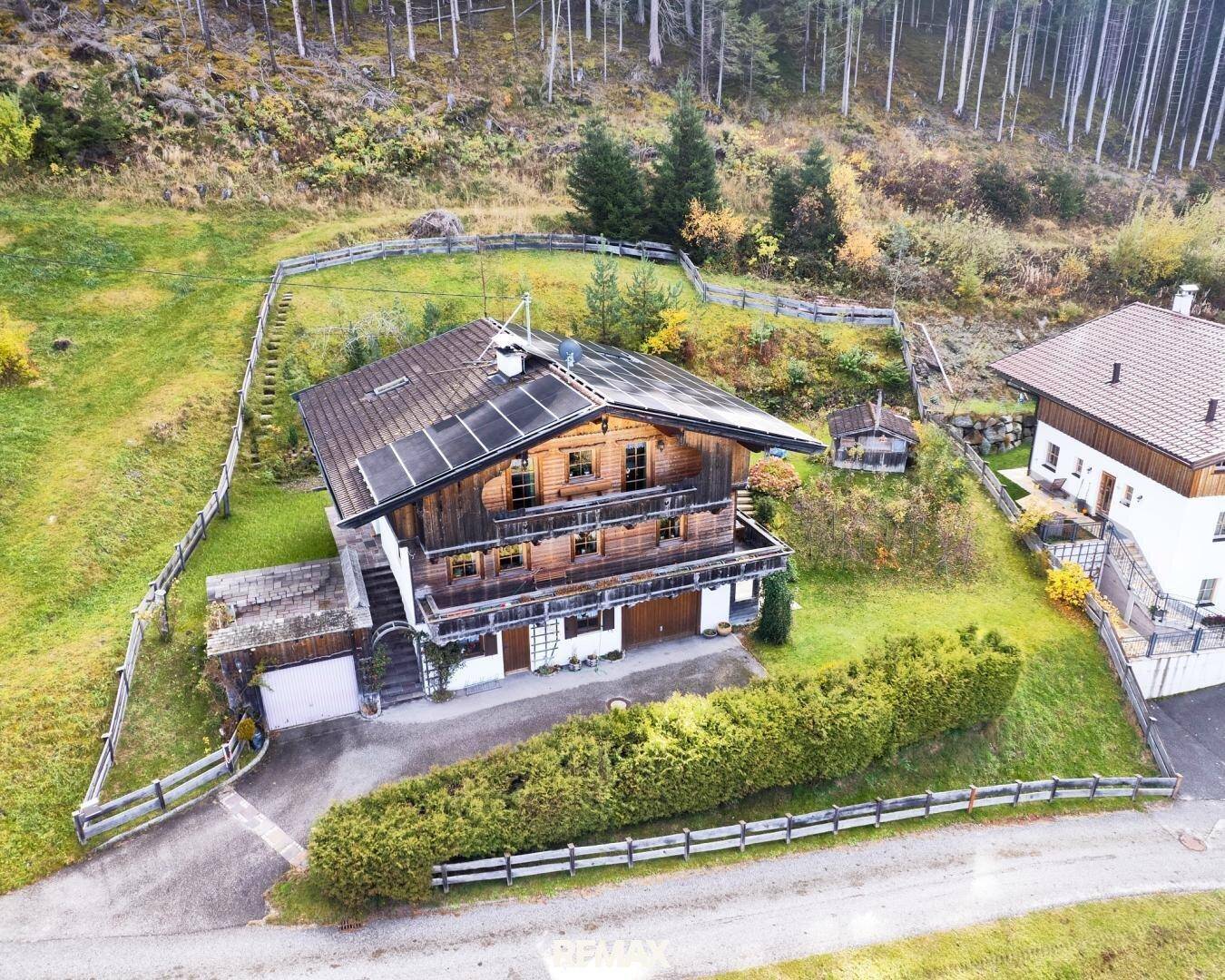 Luftaufnahme eines traditionellen Holzhauses mit Solaranlage, umgeben von Wald und Wiesen.