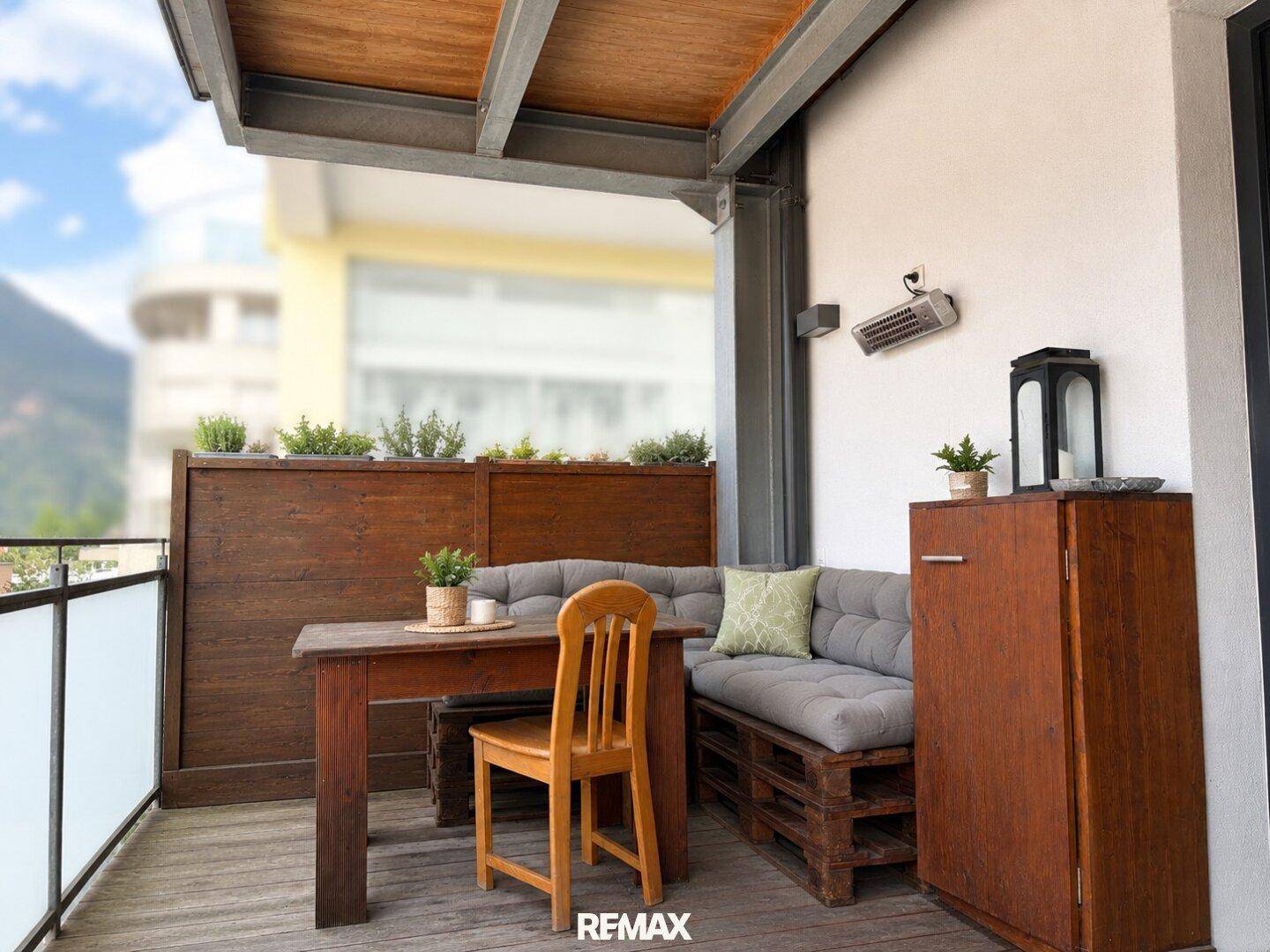 Gemütlicher Balkon mit Holzboden, Sitzgelegenheiten und Bergblick im Hintergrund.