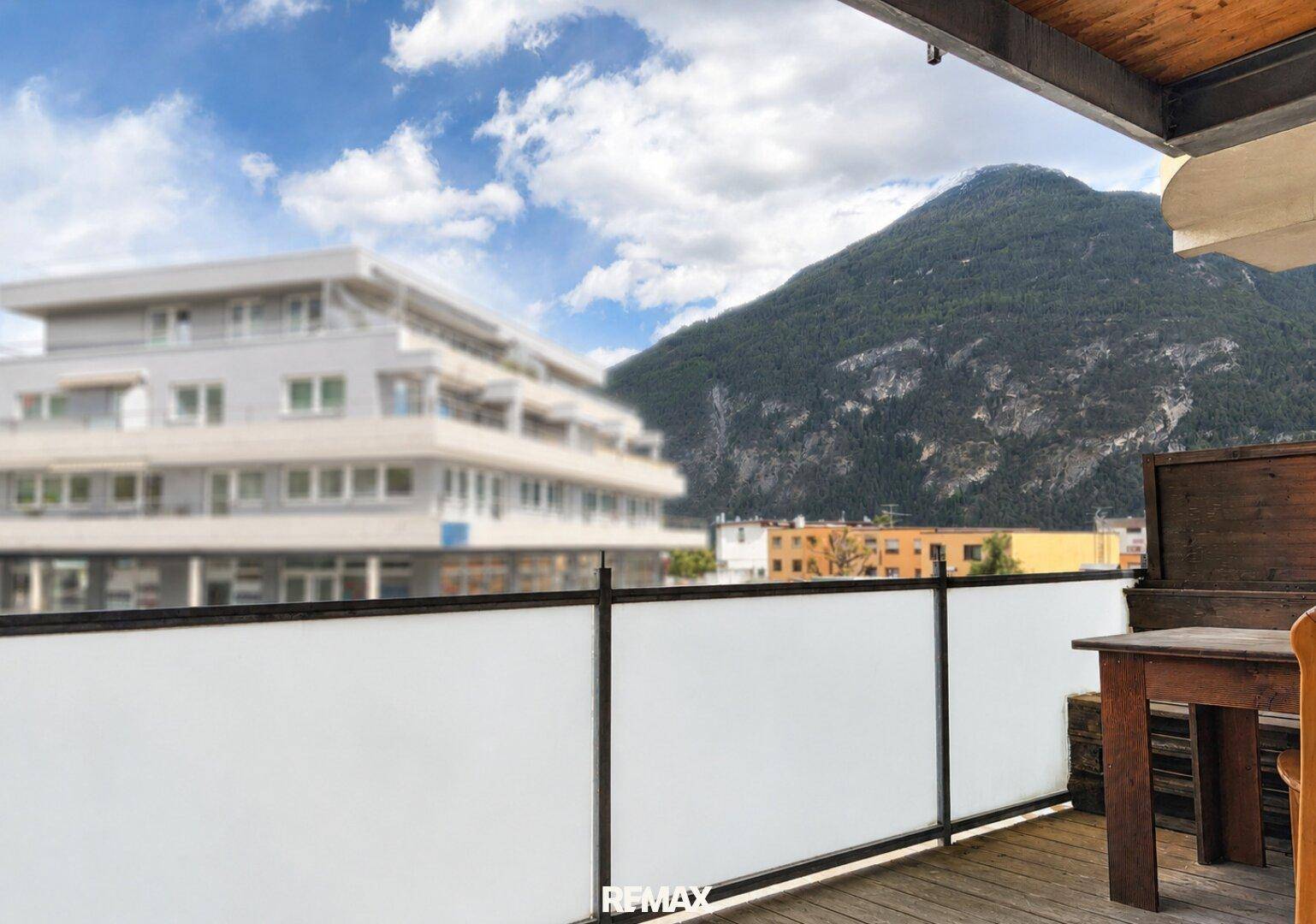 Weitblick vom Balkon auf die umliegende Berglandschaft und Gebäude.