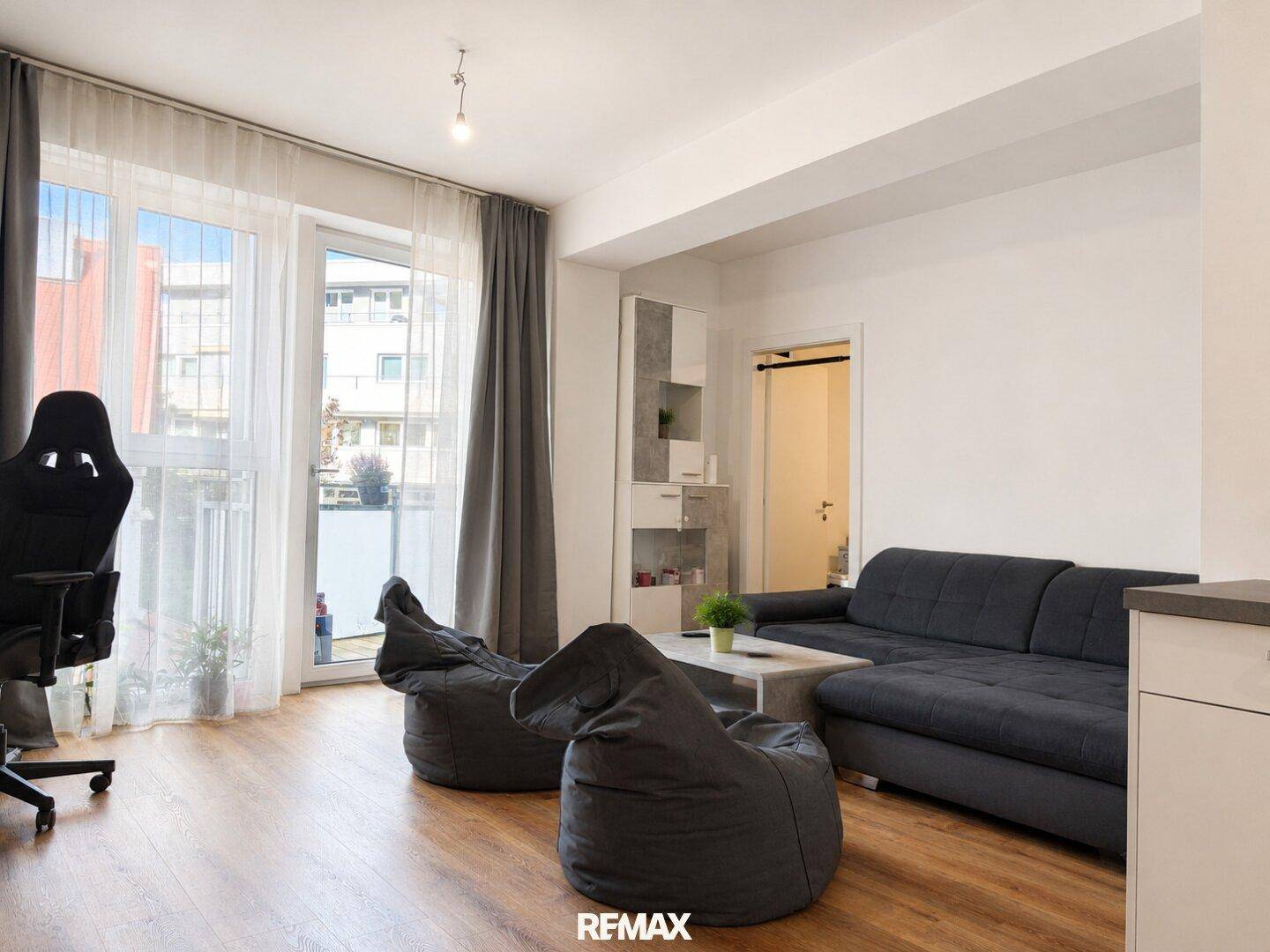 Heller Wohnbereich mit Sofa, Sitzsäcken und Zugang zu einem Balkon.