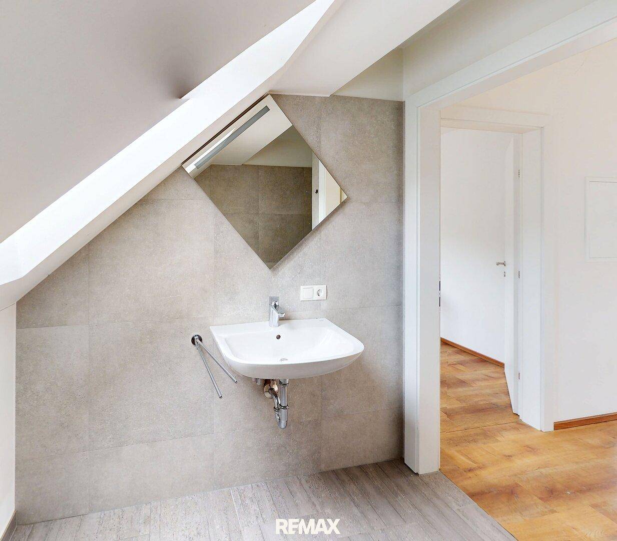 Kleines Badezimmer mit Waschbecken und Spiegel unter einer Dachschräge, modern gefliest.