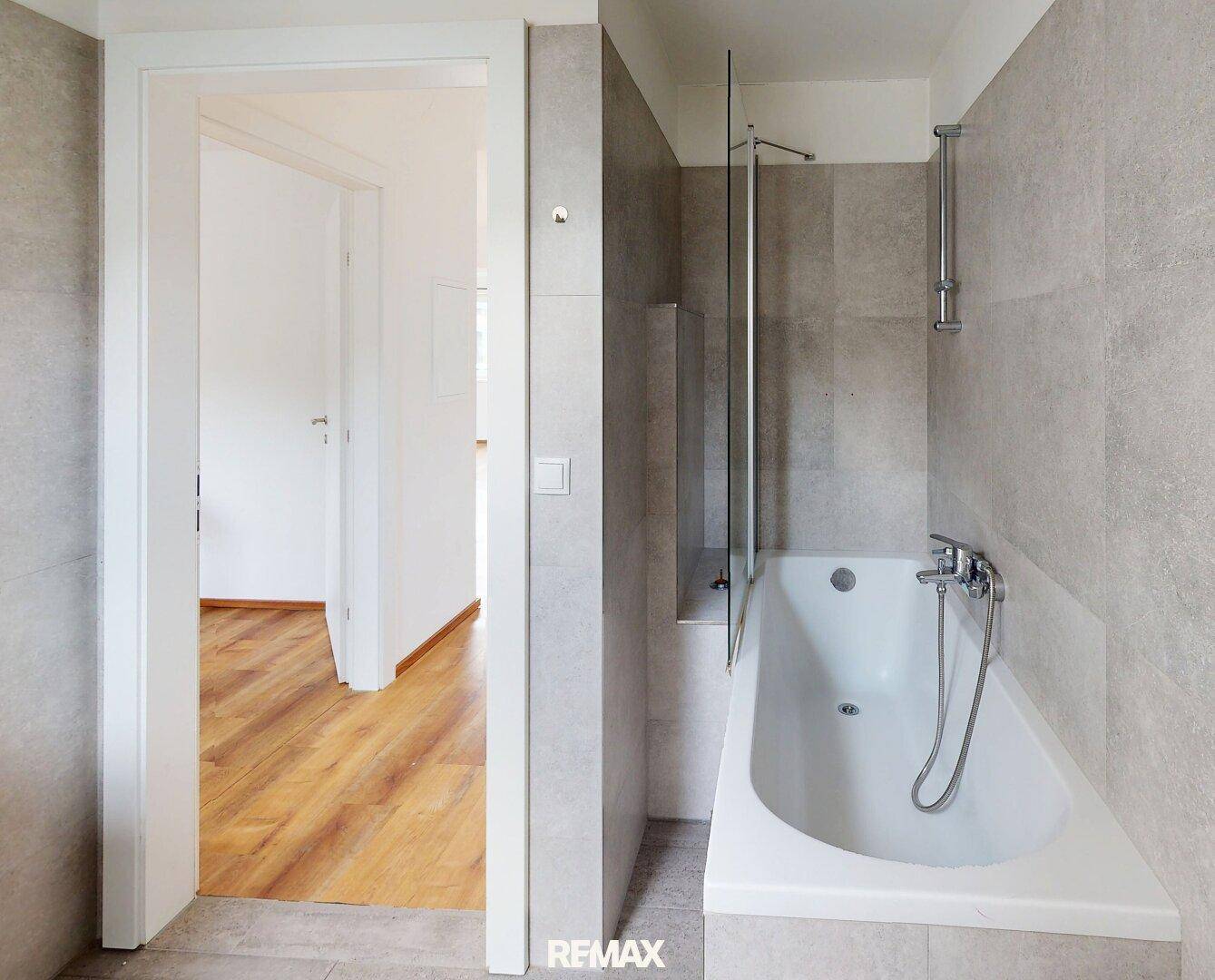 Modernes Badezimmer mit Badewanne, Duschabtrennung und grauen Wandfliesen.