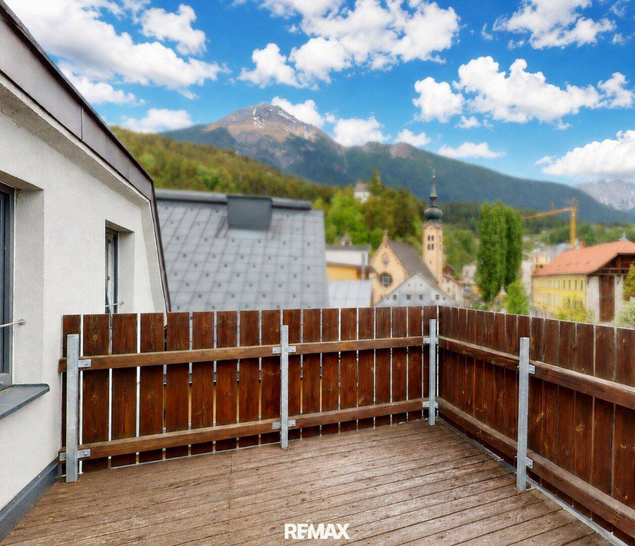 Balkon mit Holzboden und schöner Aussicht auf die umliegende Berglandschaft und Stadt.
