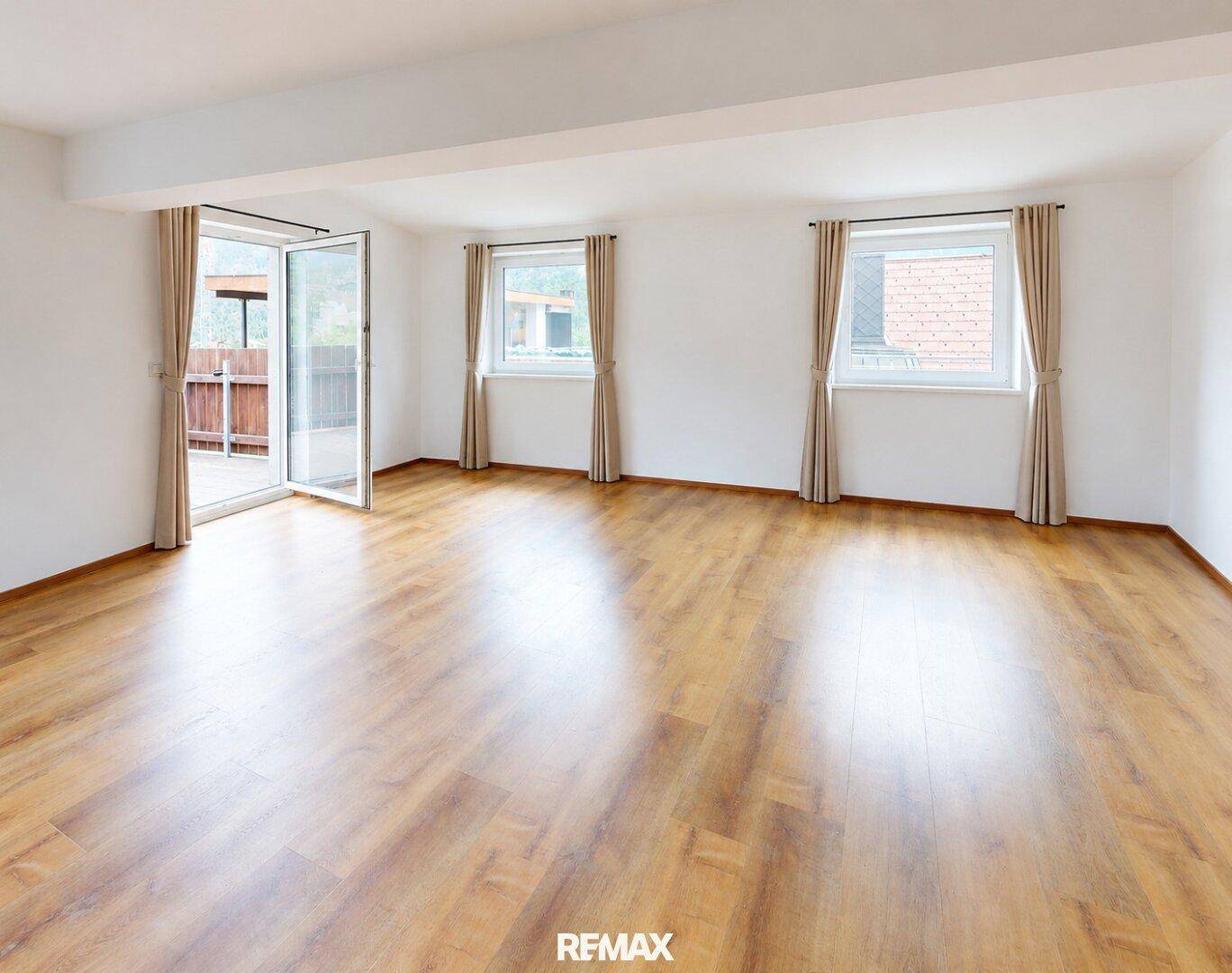Geräumiges, leeres Wohnzimmer mit hellem Holzboden und Zugang zu einem Balkon oder einer Terrasse.