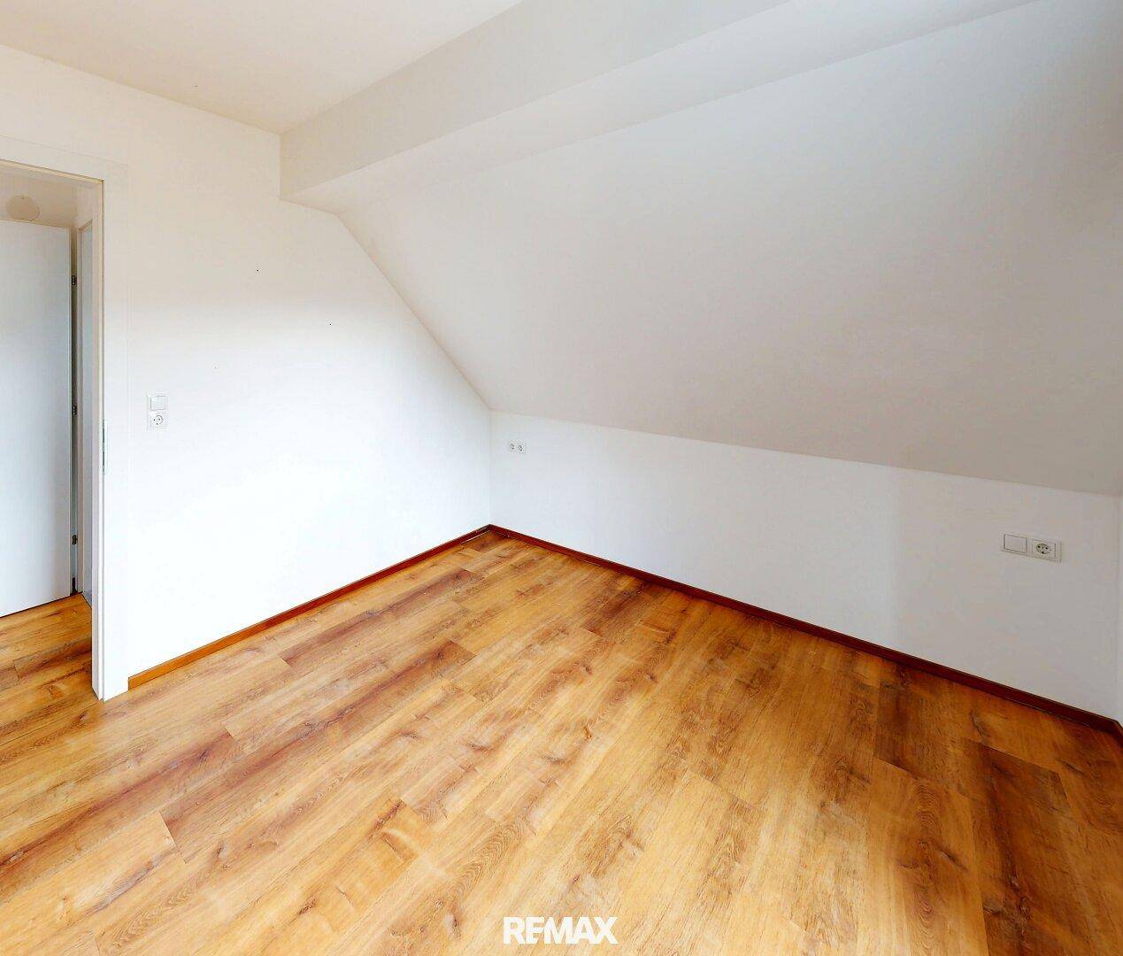 Leeres Schlafzimmer mit Holzboden und charakteristischer Dachschräge, bereit zur Gestaltung.