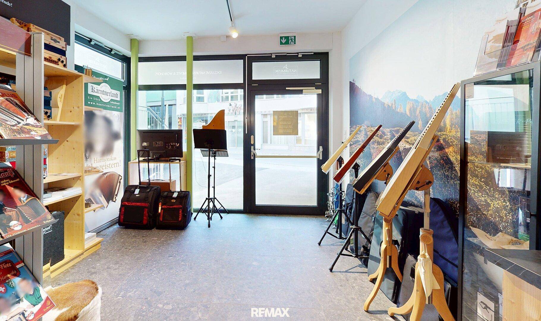 Eingangsbereich eines Geschäftsraums mit großen Glastüren, Ausstellungsregalen und Musikinstrumenten.
