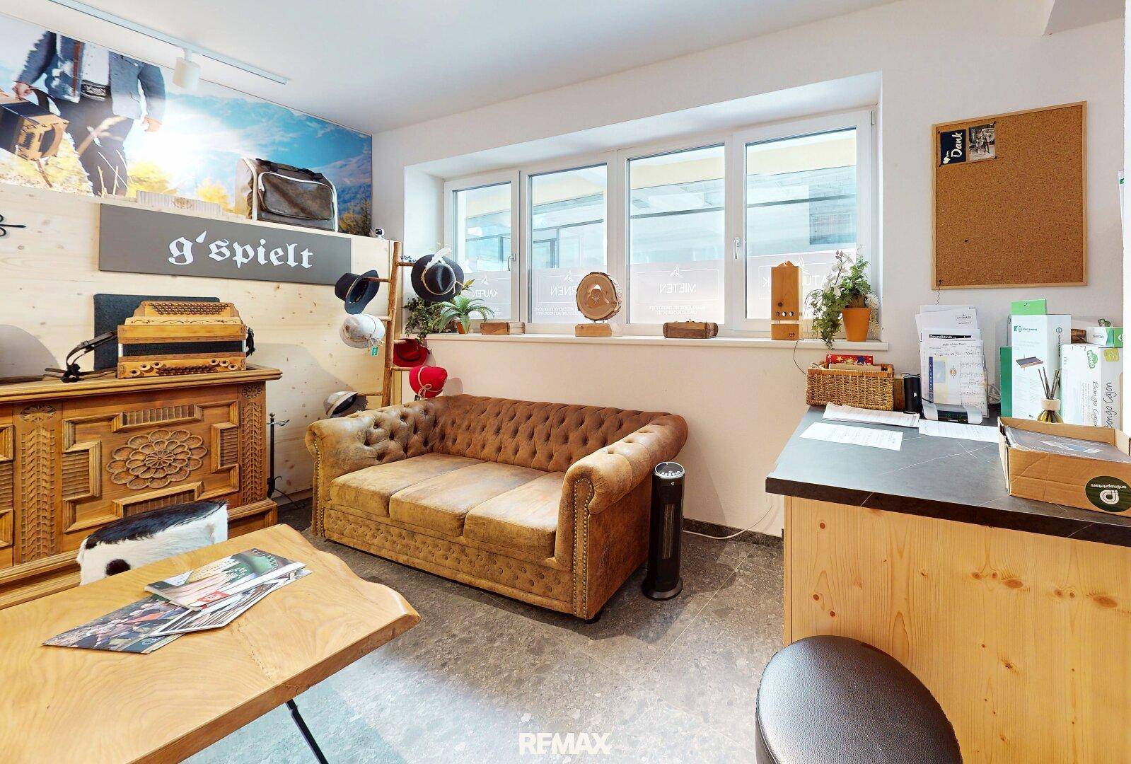 Gemütlicher Empfangsbereich oder Verkaufsraum mit bequemer Couch, Holzelementen und großen Fenstern.