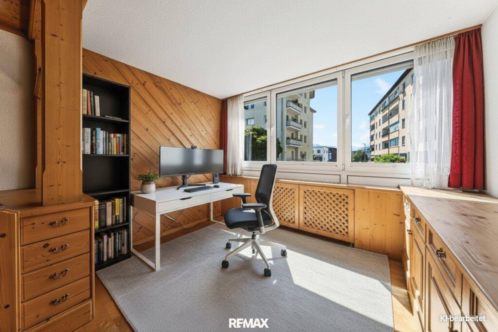 Gemütliches Arbeitszimmer mit Holzvertäfelung, großem Fenster und Blick auf die umliegenden Gebäude.