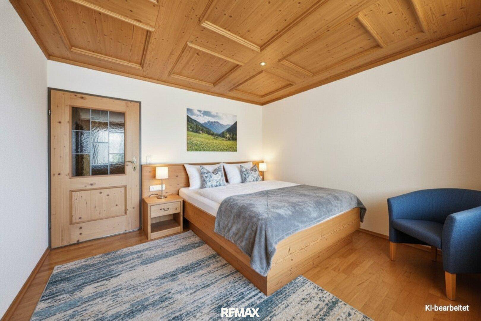 Schlafzimmer im alpinen Stil mit Holzbalkendecke, Doppelbett und einem kleinen Sessel.