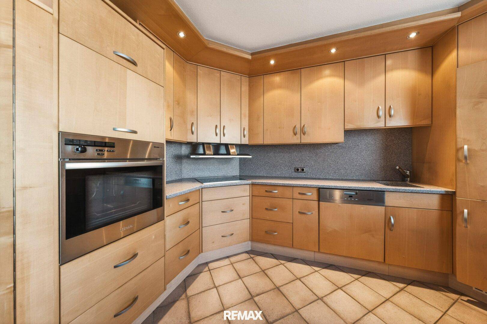 Einbauküche im traditionellen Stil mit Holzfronten, modernen Geräten und Fliesenboden.