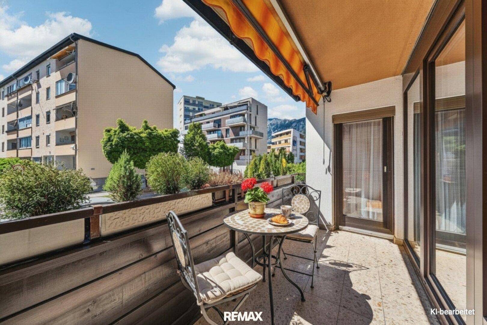 Sonniger Balkon mit kleinem Tisch, Stühlen und Blick auf die Nachbarschaft.