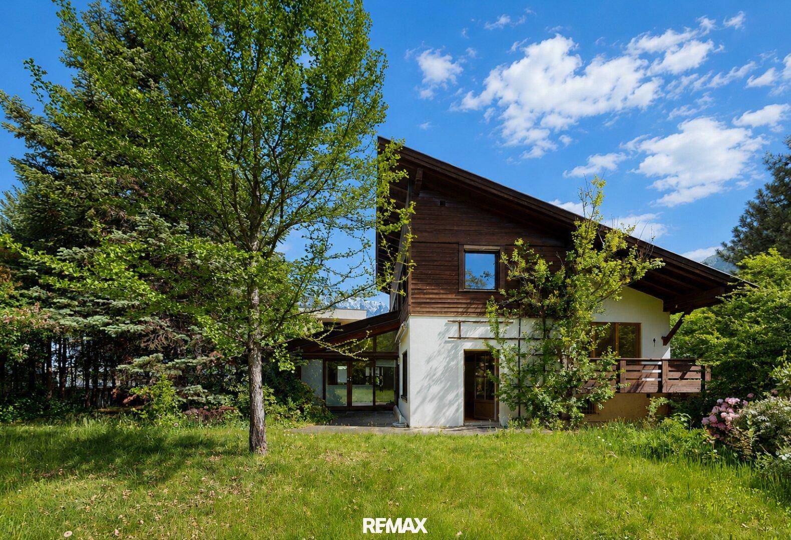 Charmantes Haus mit Holzfassade und großem Garten unter blauem Himmel.
