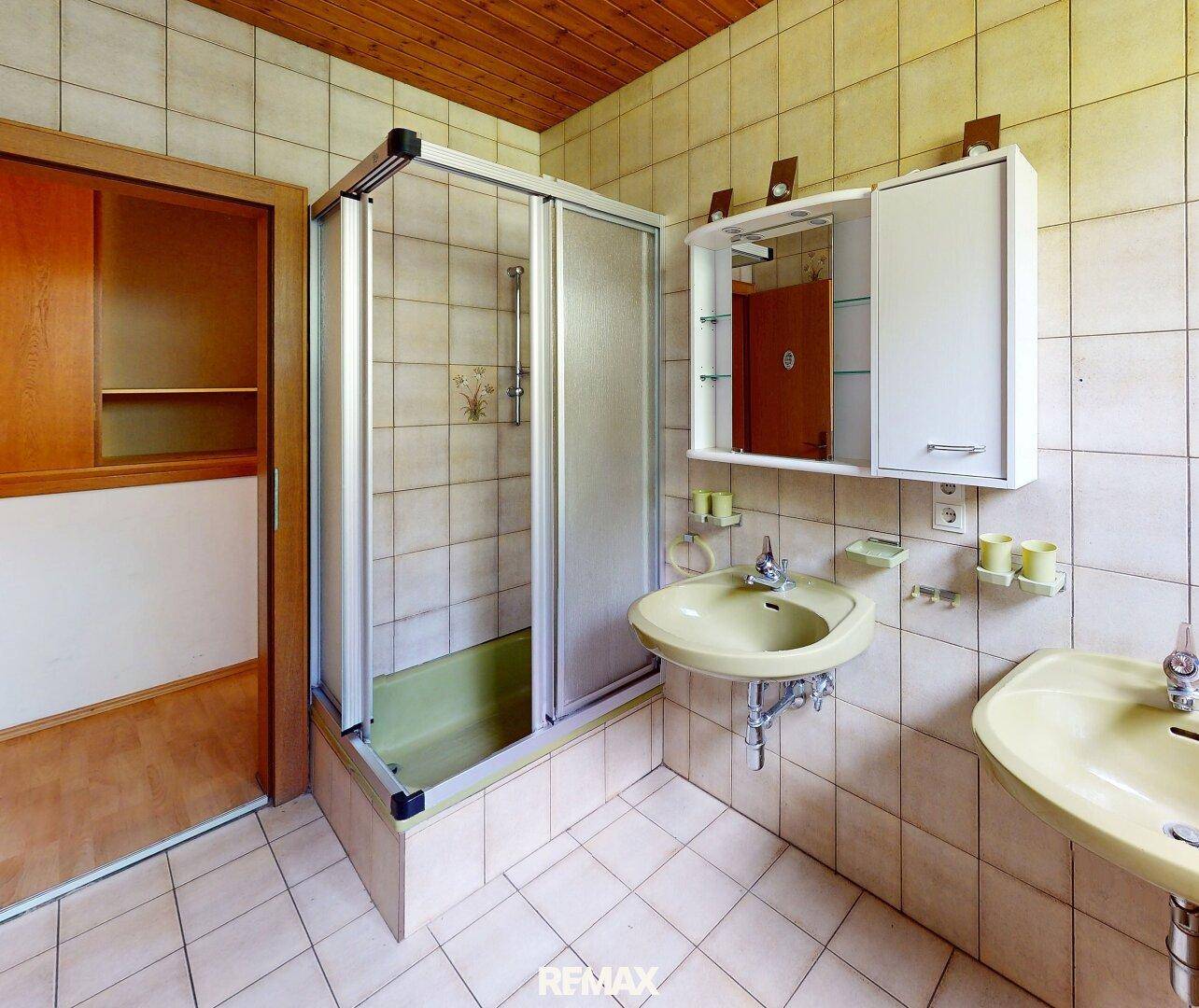 Badezimmer im 80er-Jahre-Stil mit Duschkabine, Doppelwaschbecken und Holzdecke.