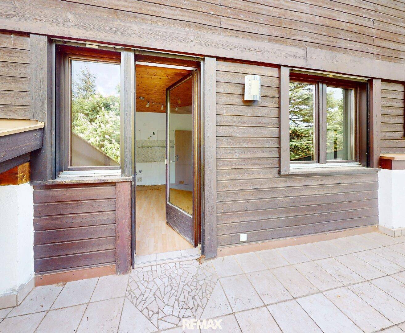 Geflieste Terrasse mit Holzwänden und Zugang zum Innenbereich des Hauses.