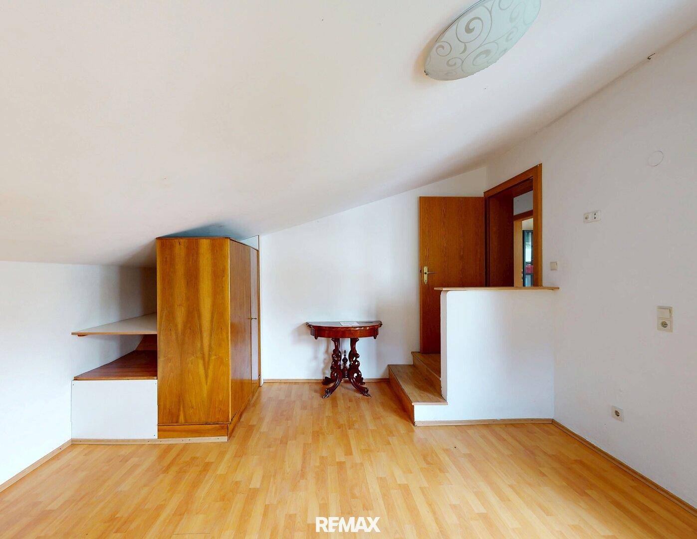 Gemütliches Zimmer im Dachgeschoss mit Holzboden, Schrank und Zugang zu weiteren Räumen.