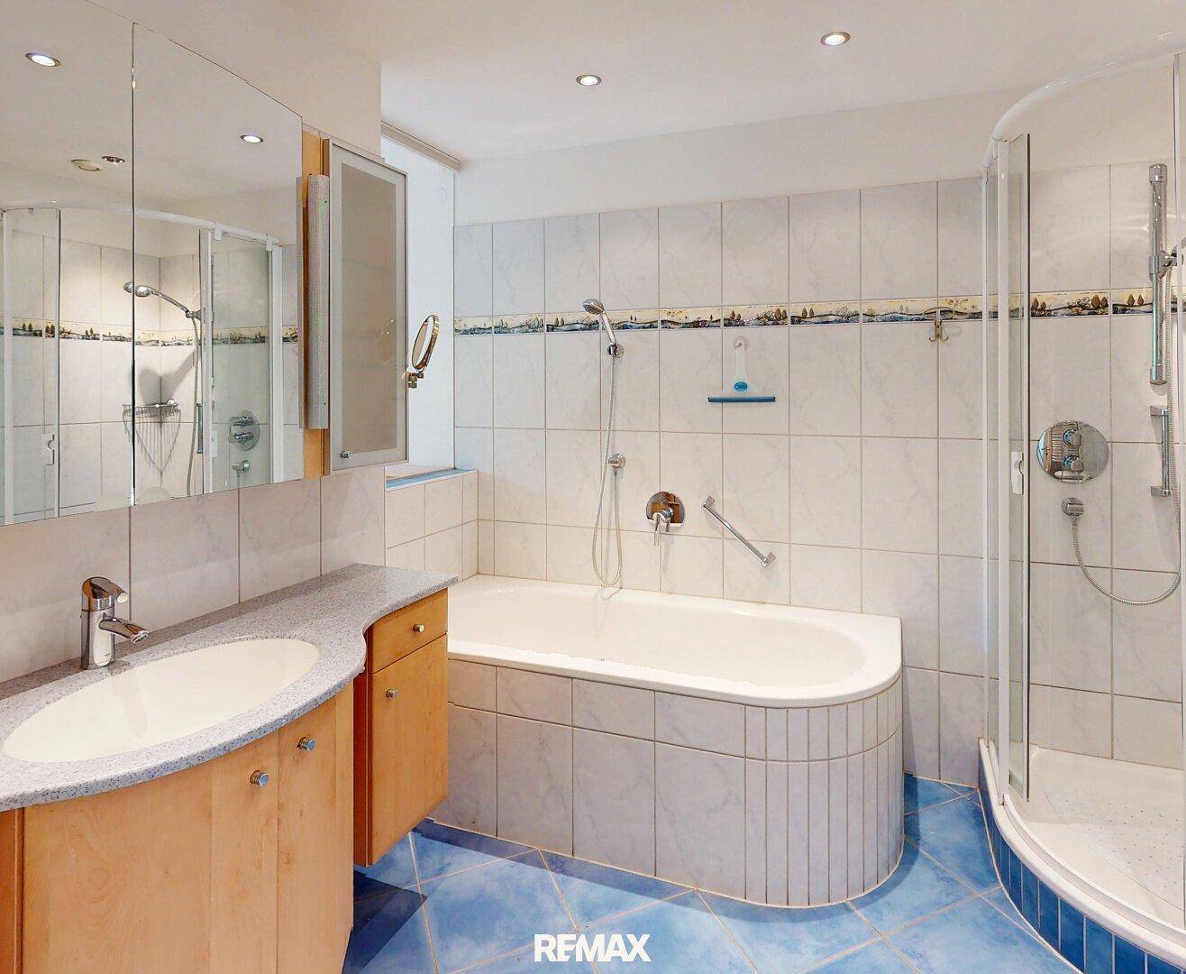 Badezimmer mit blauen Fliesen, Badewanne, Duschkabine und integriertem Spiegelschrank.