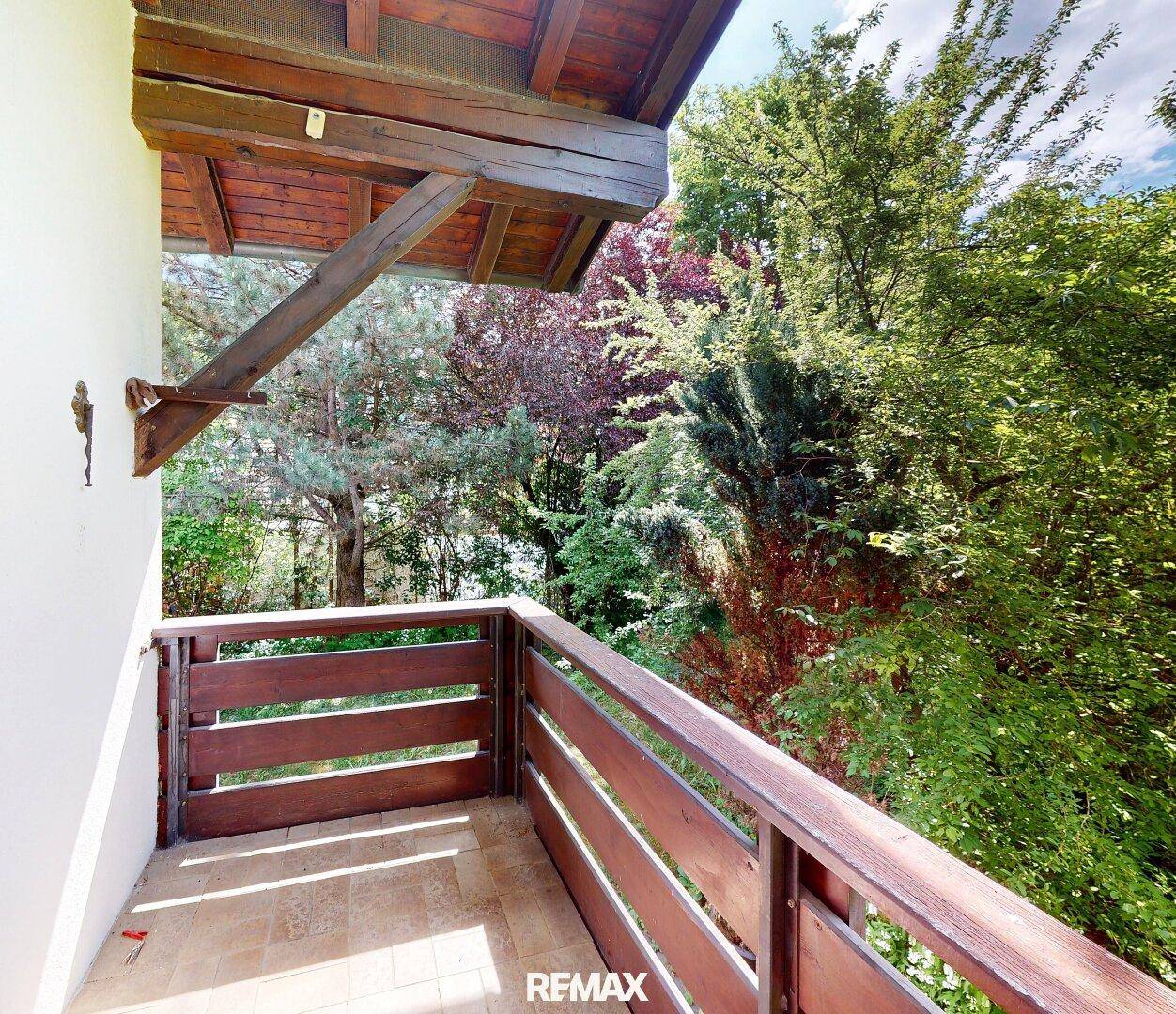Gemütlicher Balkon mit Holzbalken und Geländer, umgeben von üppigem Grün.
