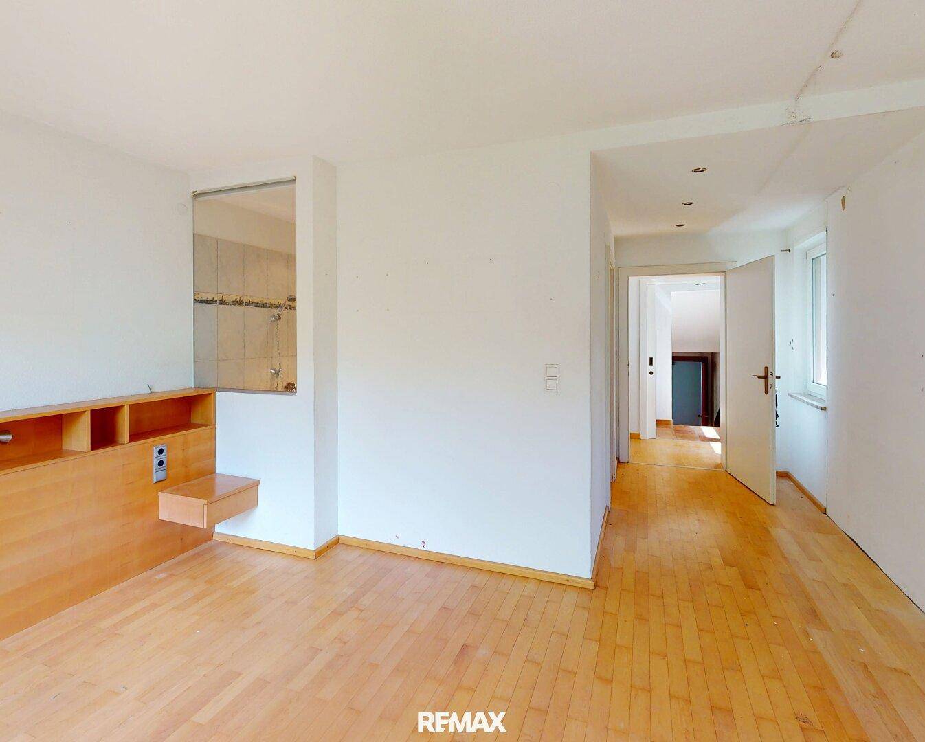 Helles Schlafzimmer mit Holzboden und offenem Zugang zu einem Duschbereich.