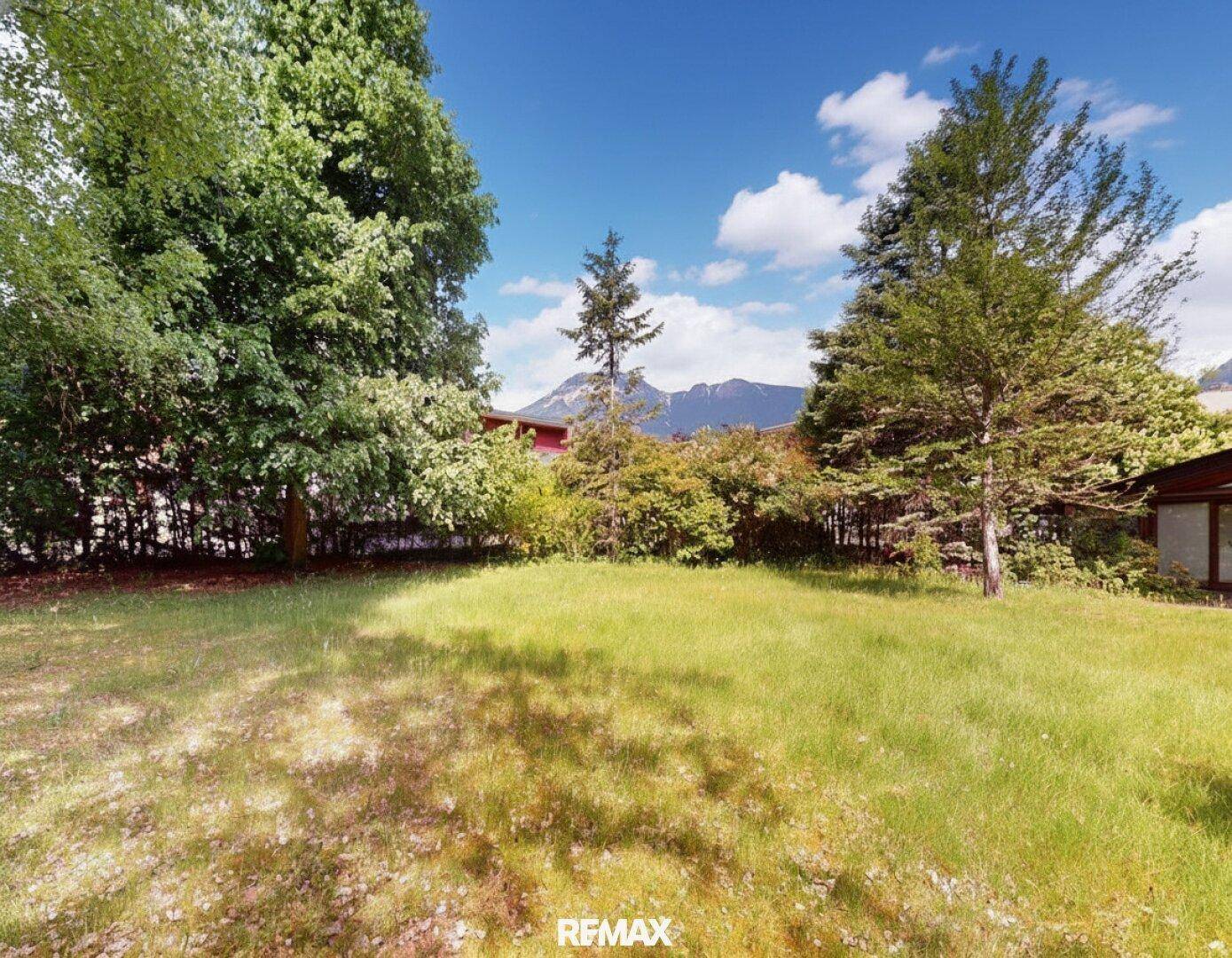 Großer, gepflegter Gartenbereich mit Rasenfläche, hohen Bäumen und Bergblick im Hintergrund.