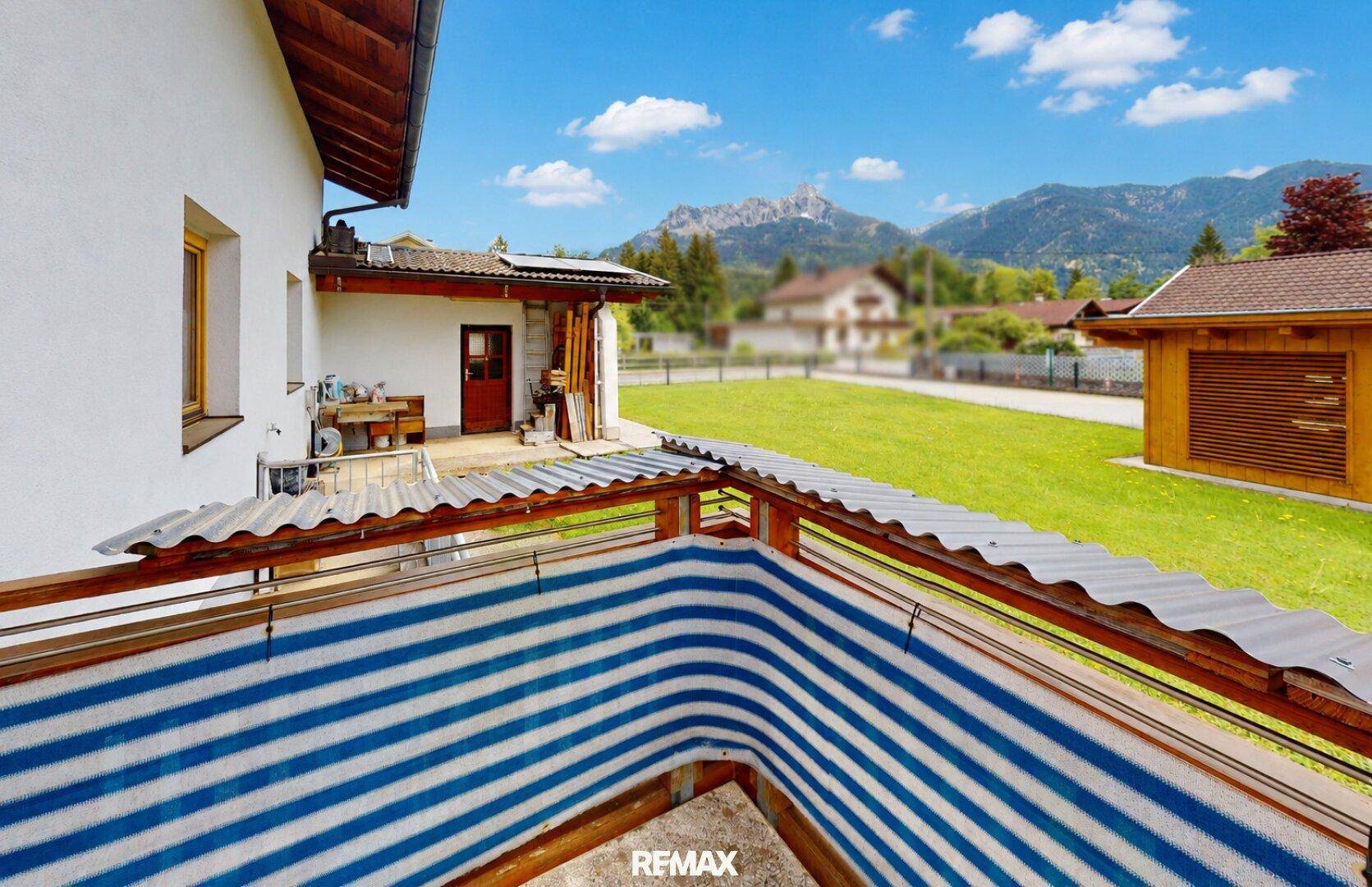 Überdachter Balkon mit blau-weiß gestreiftem Sichtschutz und weitem Blick in die Natur.
