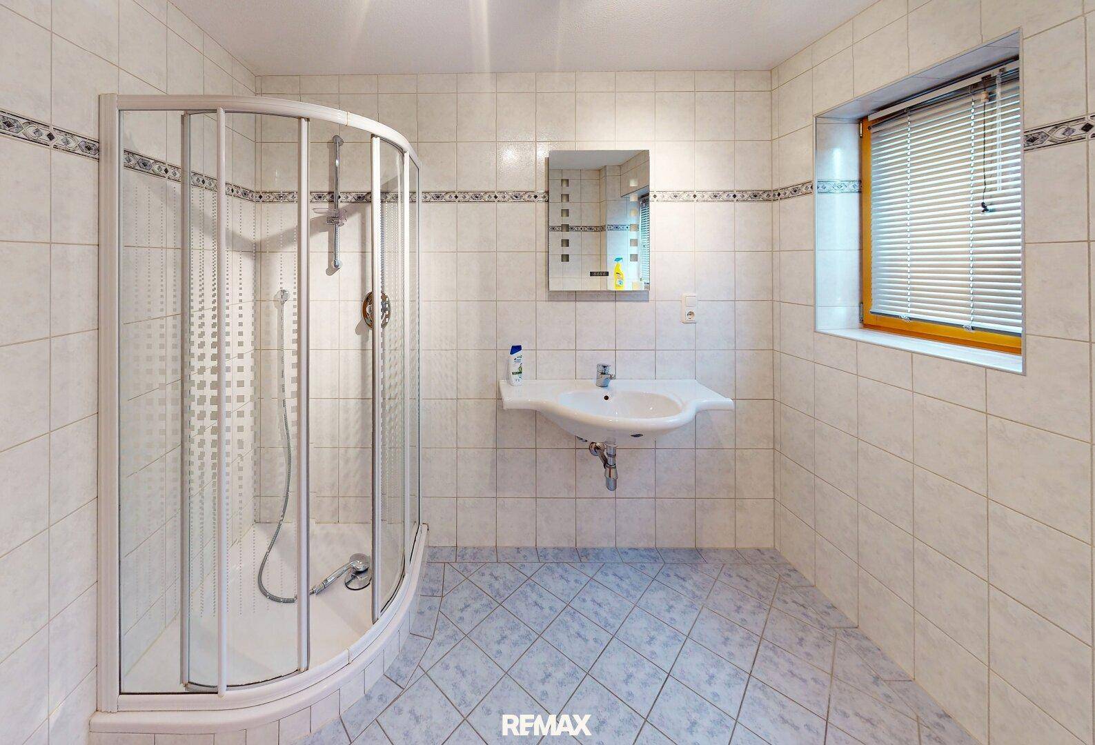 Helles Badezimmer mit Duschkabine, Waschbecken und Fenster, komplett gefliest.