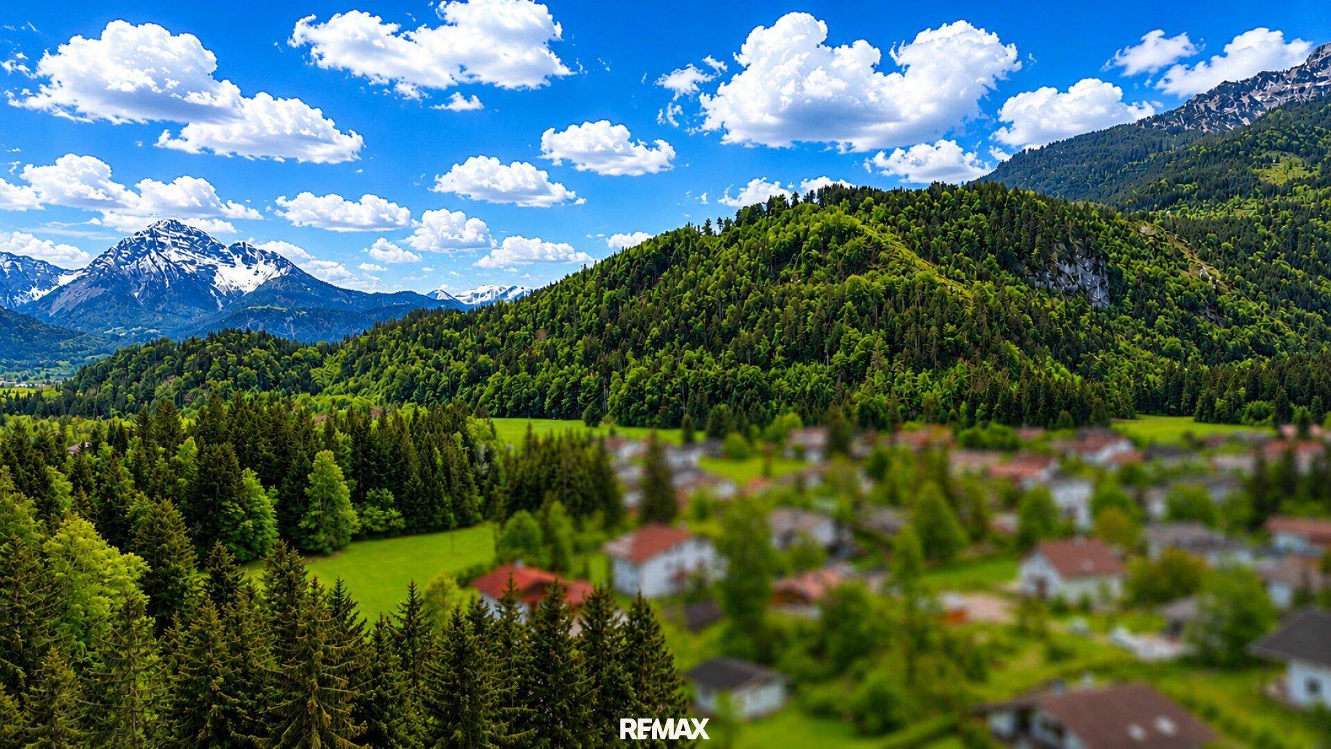 Panoramablick auf eine ländliche Siedlung umgeben von grünen Wäldern und Bergen.
