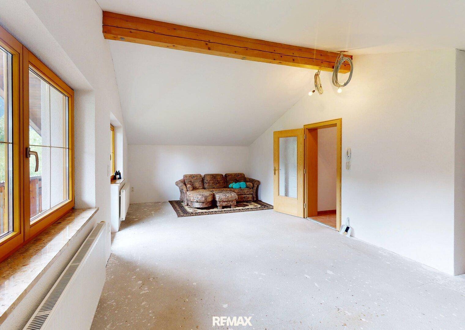 Geräumiges Wohnzimmer im Umbau mit Holzbalken und großen Fenstern, bereit für neue Böden.