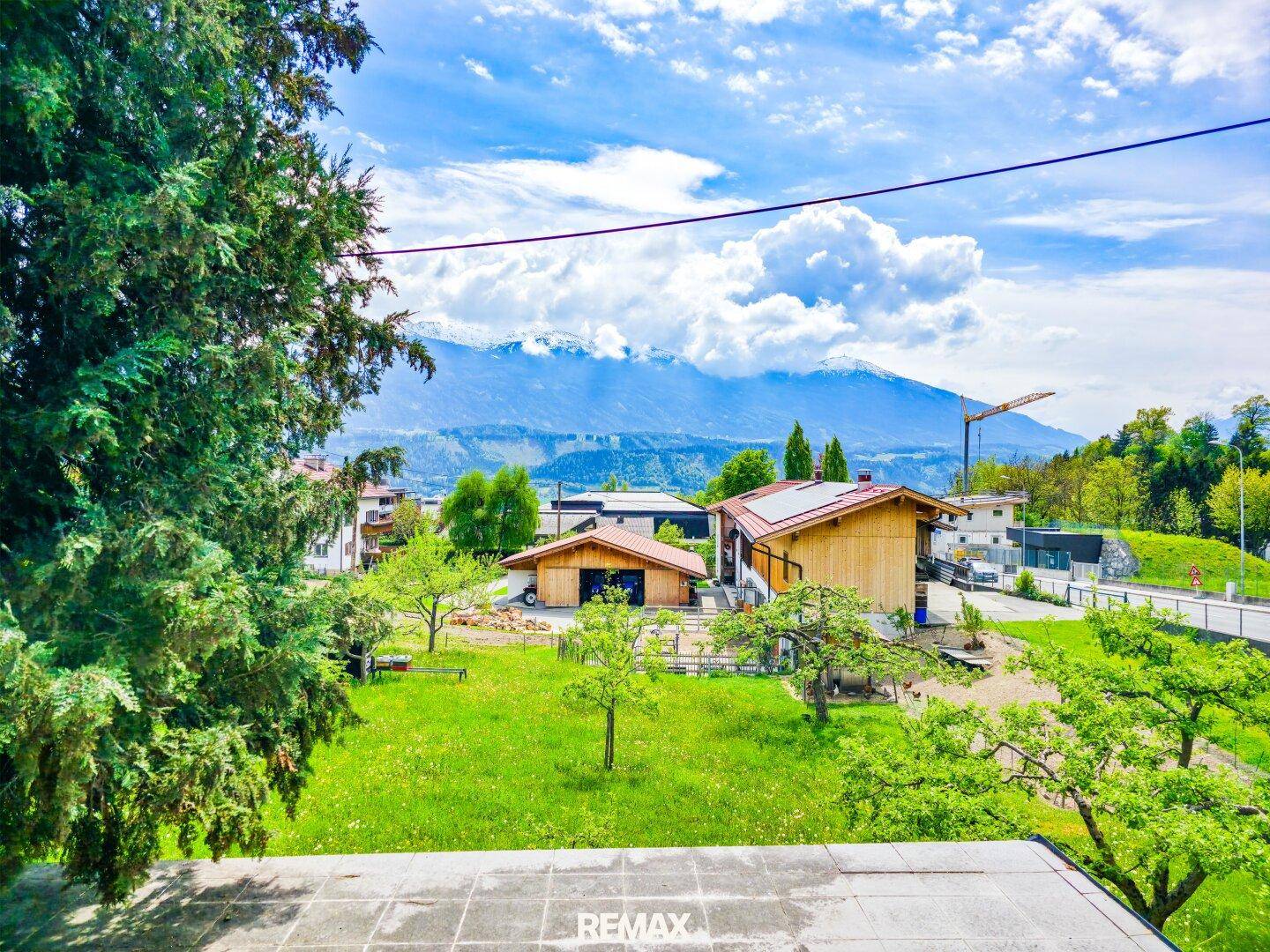 Weitläufiger Blick über eine grüne Landschaft mit Häusern und majestätischen Bergen im Hintergrund.