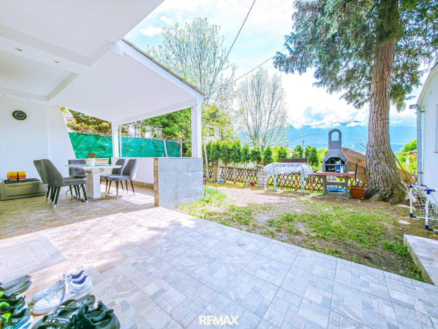 Gartenbereich mit überdachter Terrasse, Rasenfläche und Grillplatz, umgeben von Natur und Bergblick.