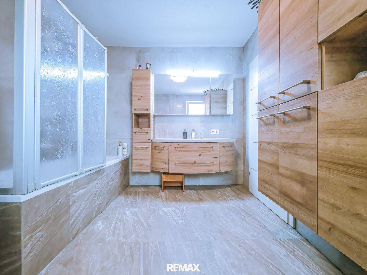 Geräumiges Badezimmer mit Holzwaschtisch, großem Spiegel und einer Dusch-Badewannen-Kombination.