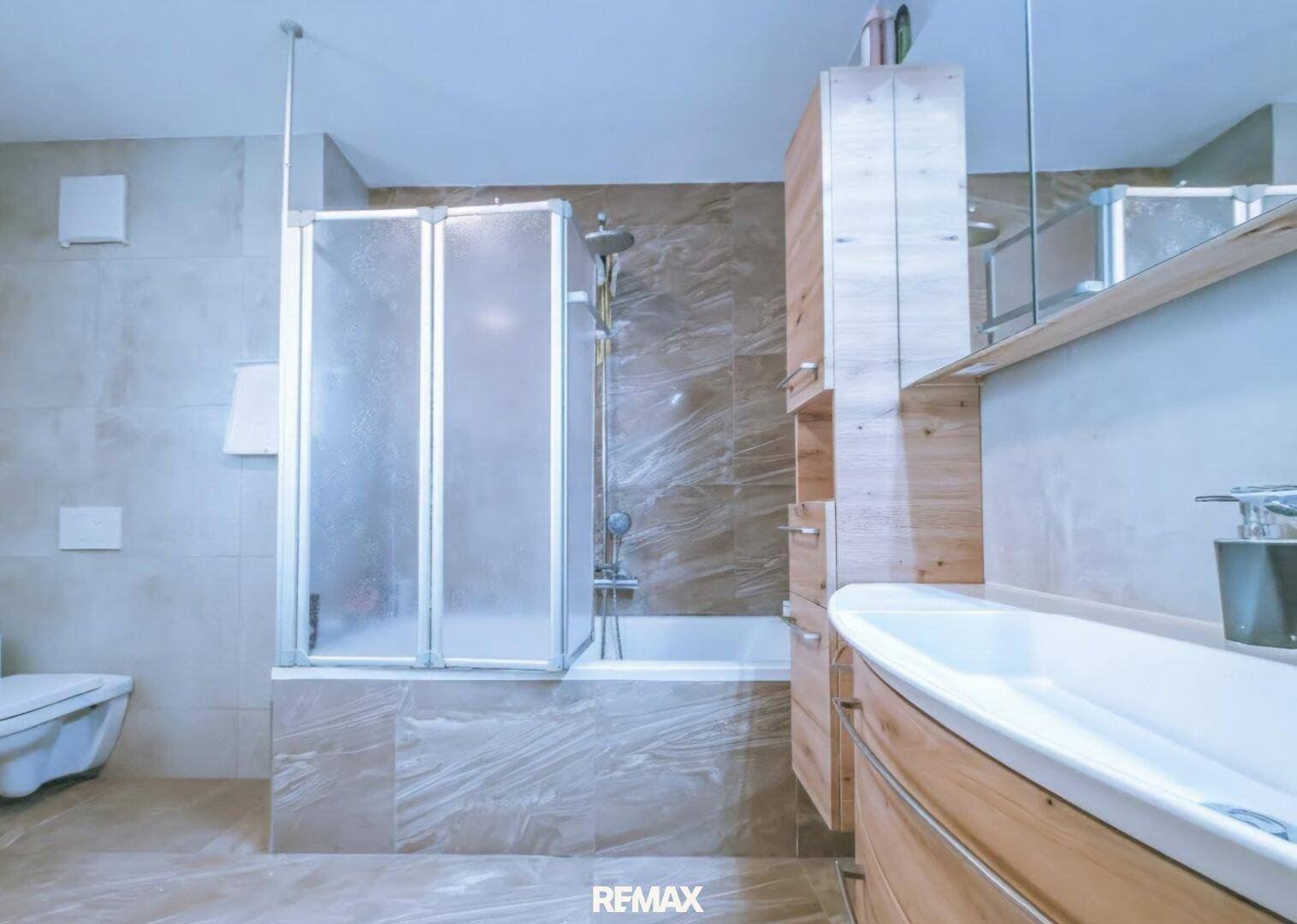 Modernes Badezimmer mit Dusch-Badewannen-Kombination, Wand-WC und eleganten Fliesen.