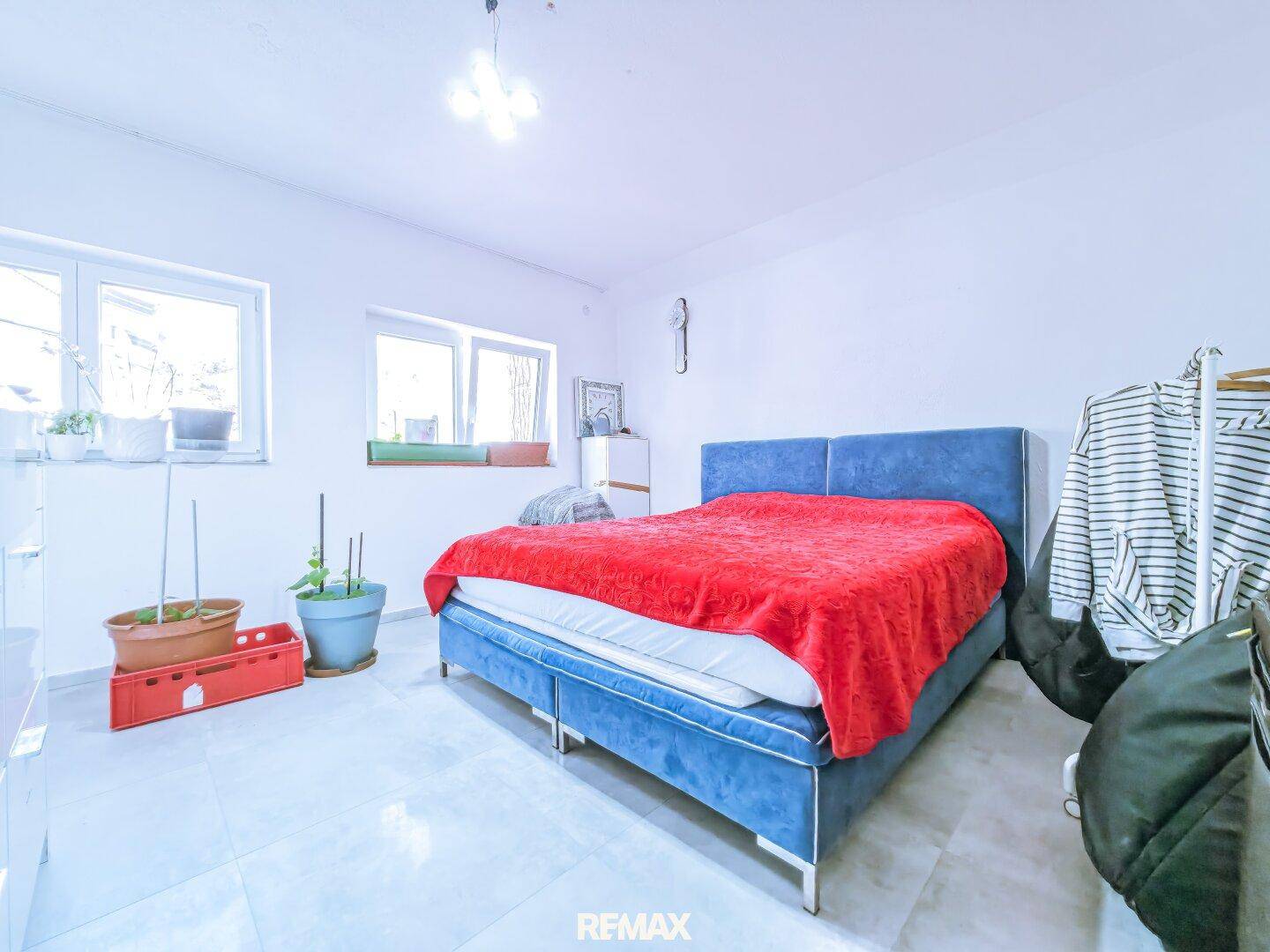Helles Schlafzimmer mit blauem Polsterbett, weißen Wänden und Fliesenboden, gut beleuchtet.