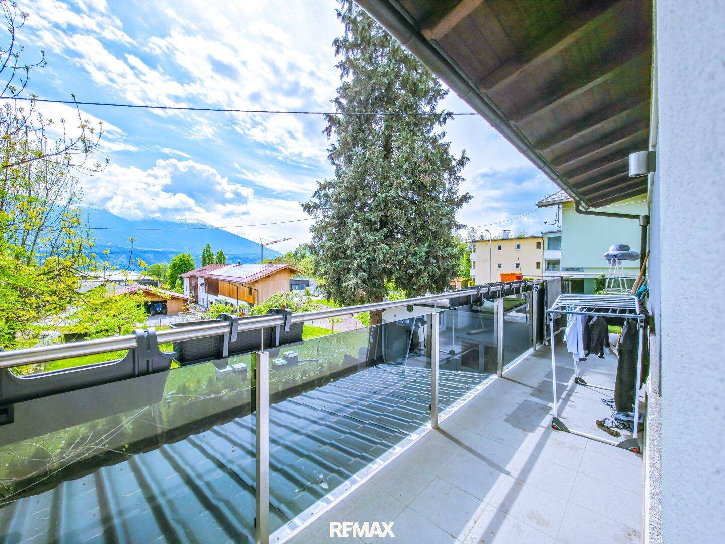 Langer Balkon mit Glasgeländer, Wäscheständer und weitem Blick auf die umliegenden Berge.
