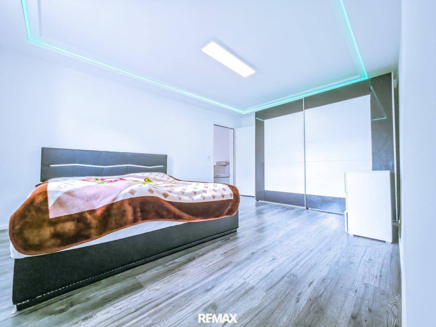 Modernes Schlafzimmer mit großem Bett, Einbauschrank und dekorativer Deckenbeleuchtung.