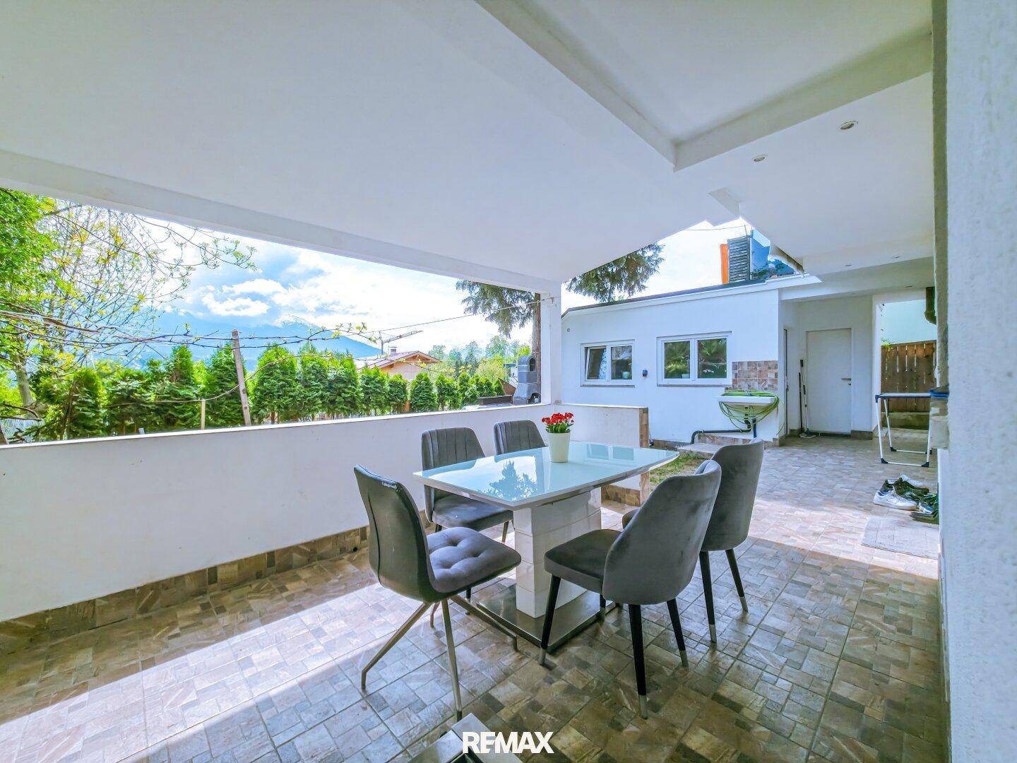 Überdachte Terrasse mit Esstisch und Stühlen, bietet einen schönen Bergblick und Fliesenboden.