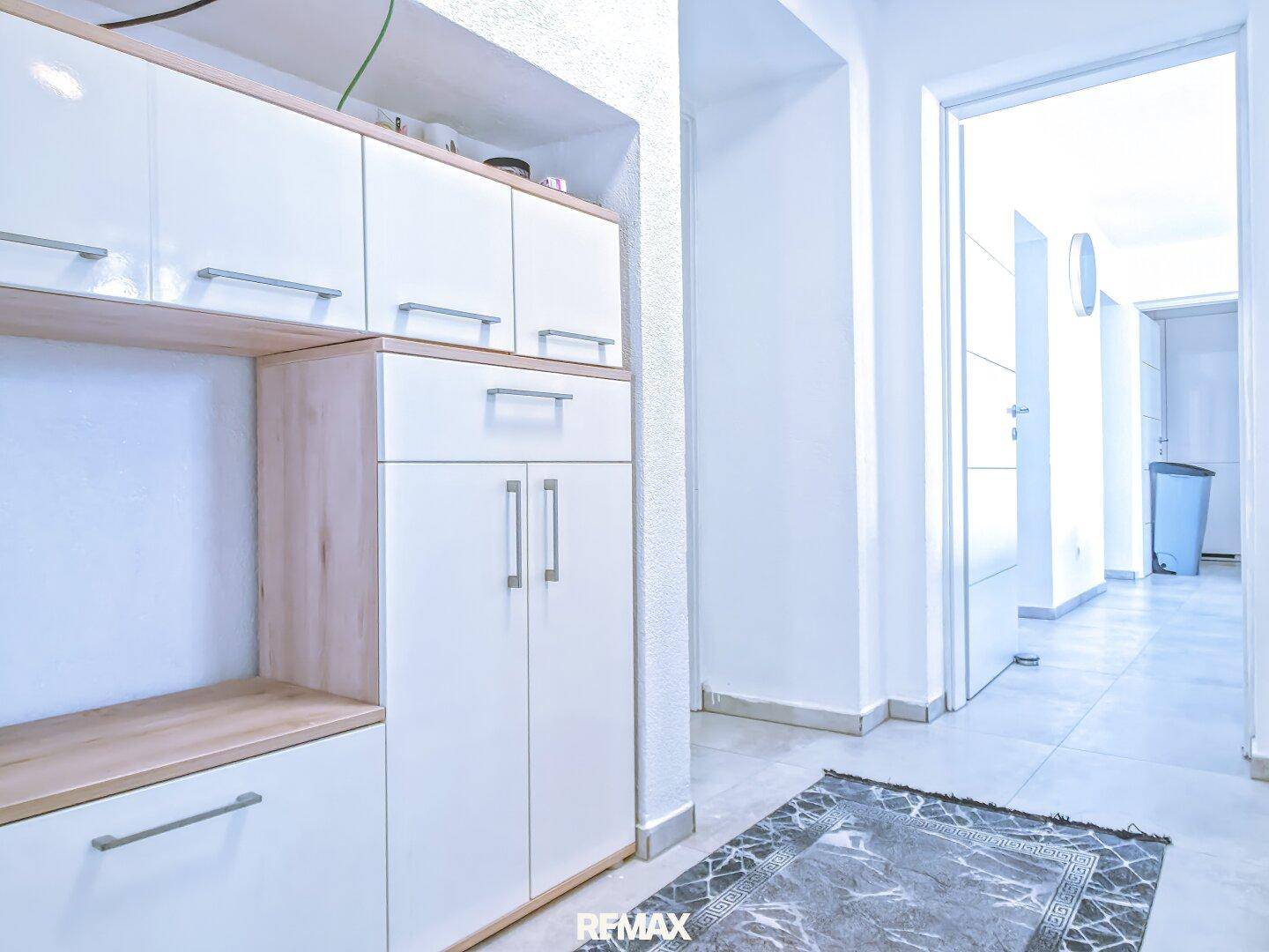 Heller Flur mit praktischen weißen und holzfarbenen Einbauschränken und Fliesenboden.